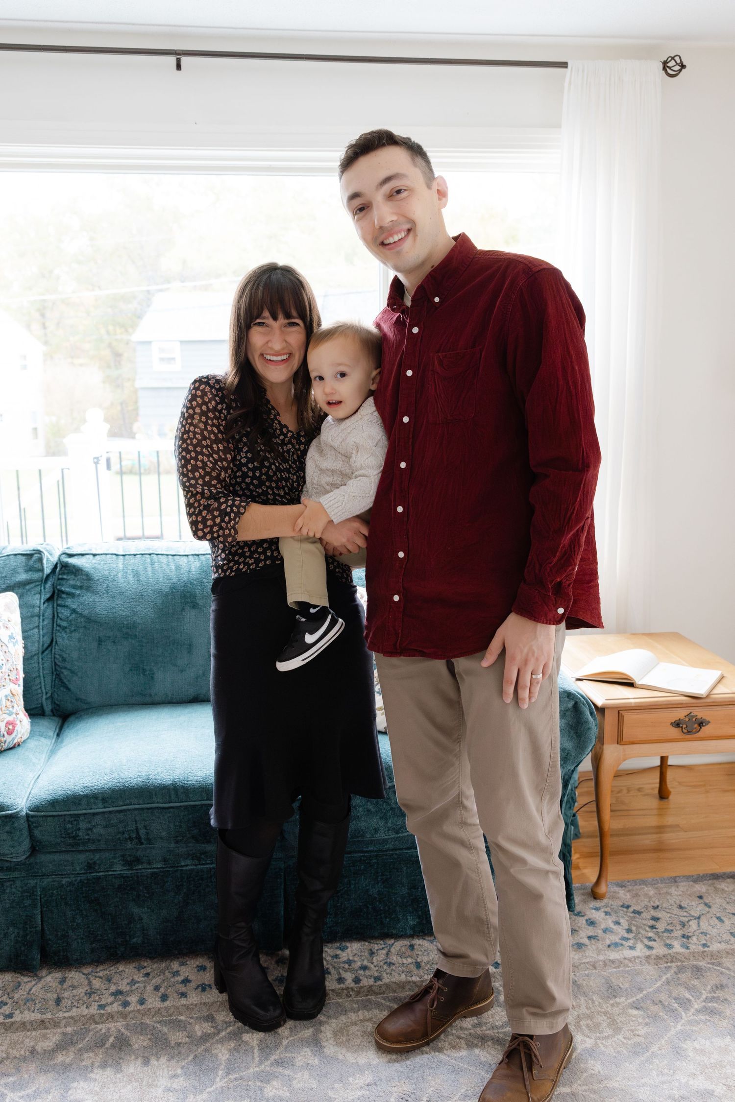 A family poses together in front of a teal couch in a bright living room during a photo session.