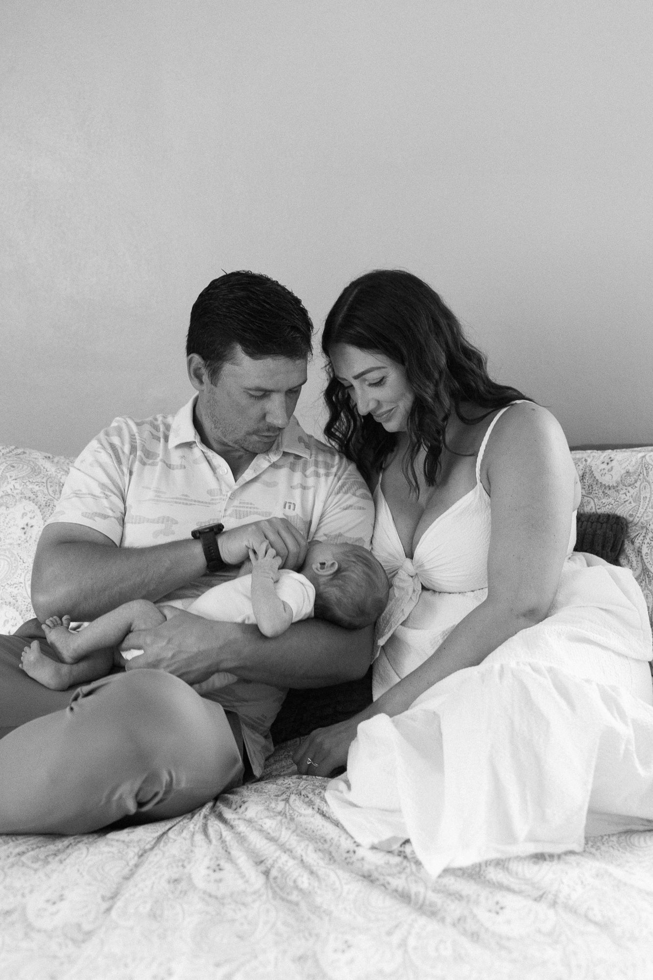 black and white photo of newborn parents holding newborn baby while sitting on bed