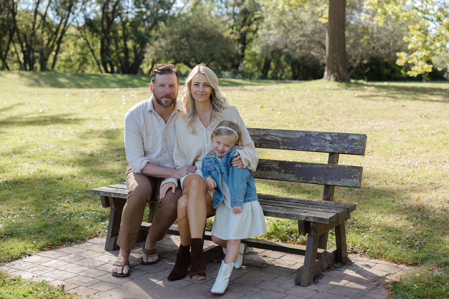 A family sits together on a wooden bench in a sunny park on a beautiful spring day.
