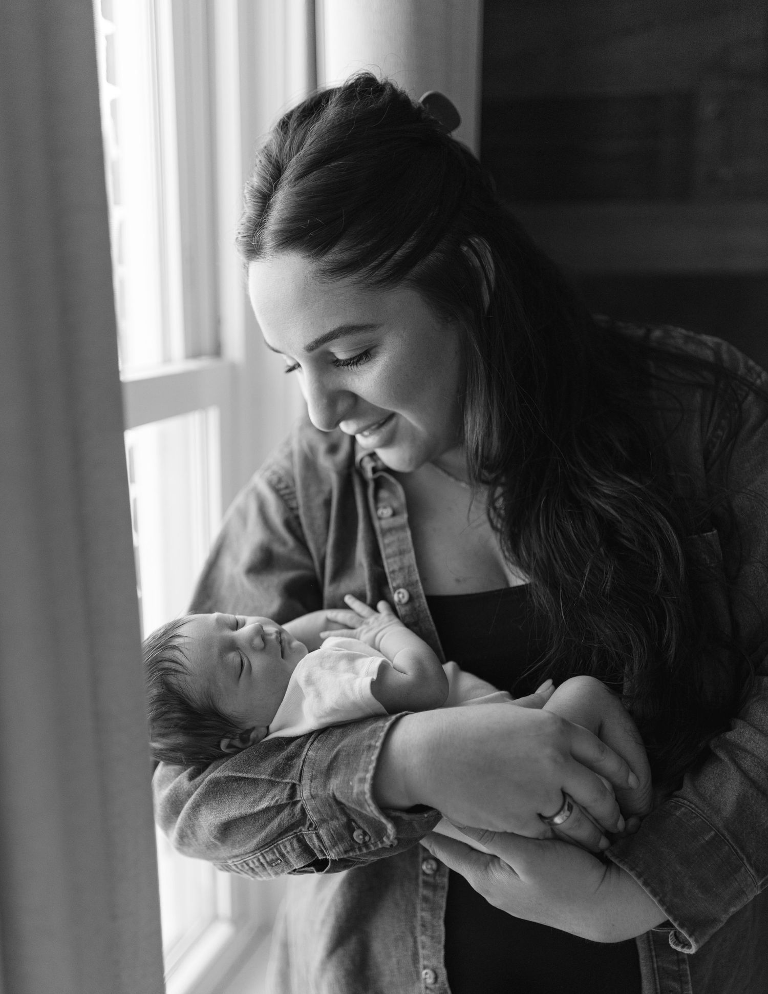 A series of black and white photos showing tender moments between a parent and infant in front of a window.