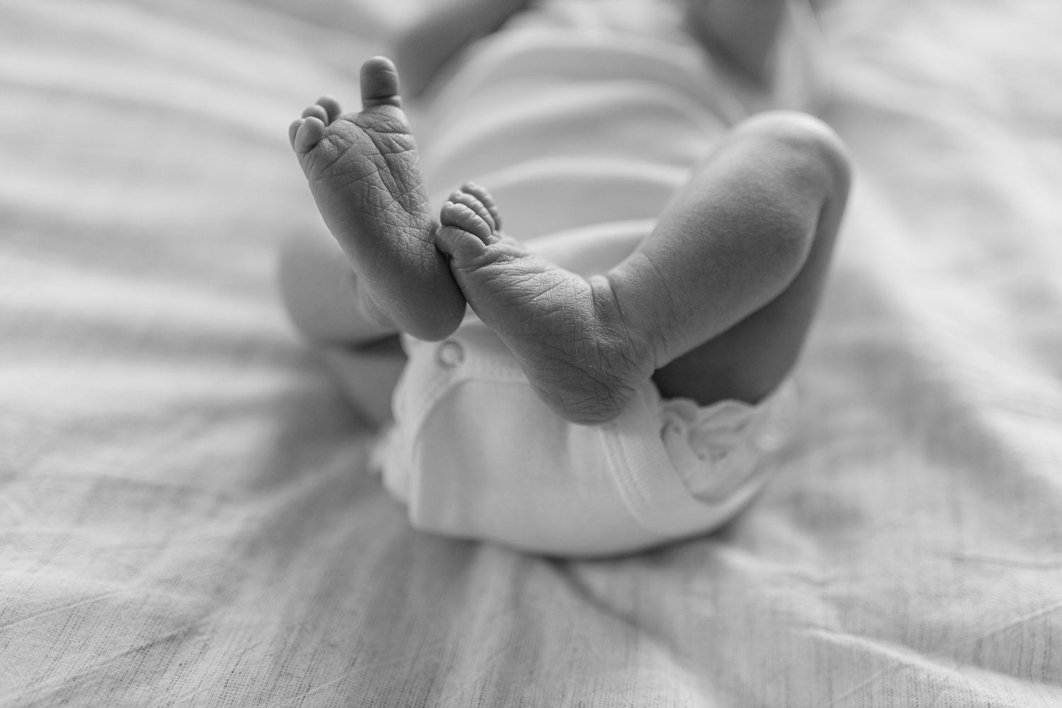 Baby feet on white bed sheets resting comfortably in soft natural light, black and white photograph.