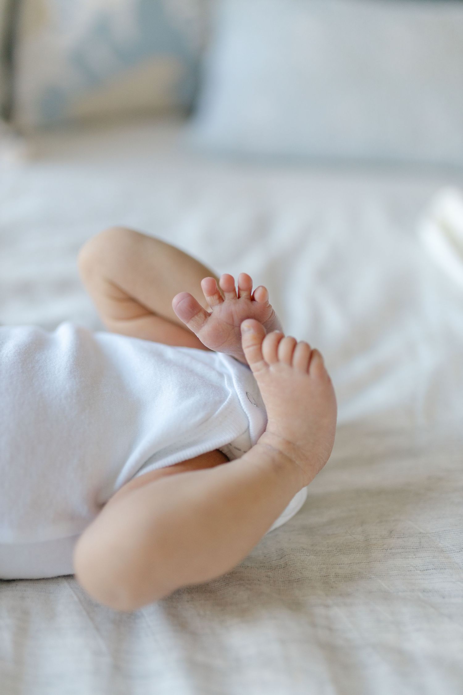Close-up of tiny baby feet resting on white bedding, showing delicate toes and soft skin in natural light.