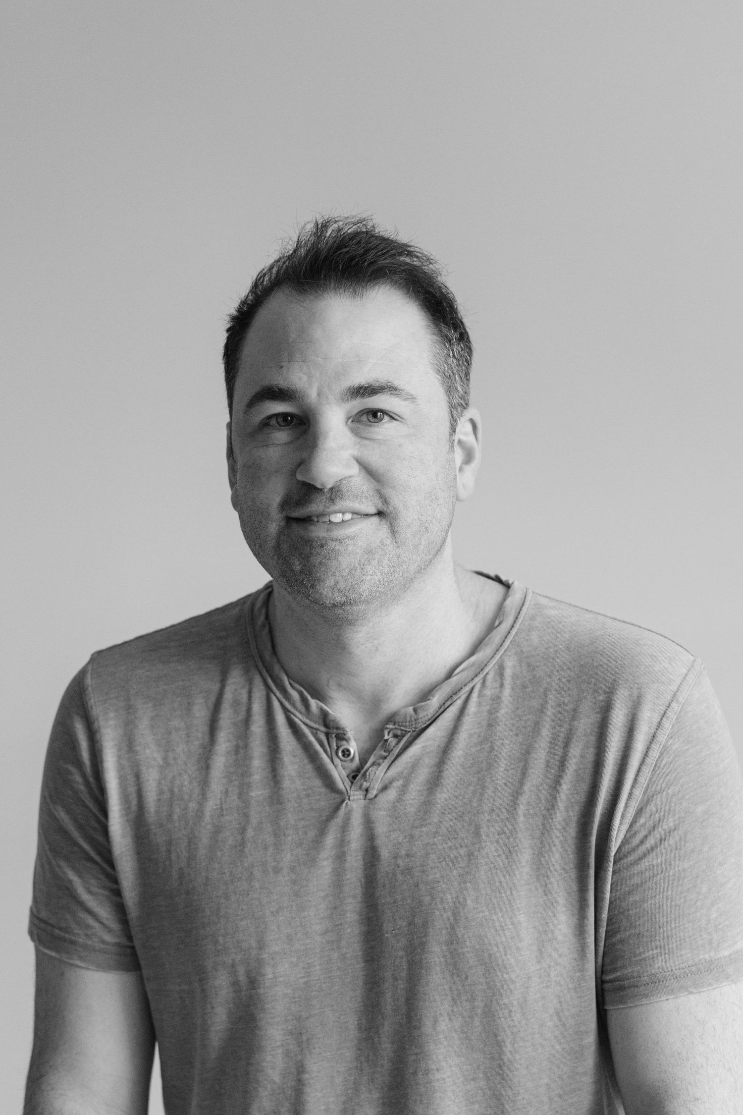 Black and white portrait of a person in a casual grey henley shirt smiling against a light background.