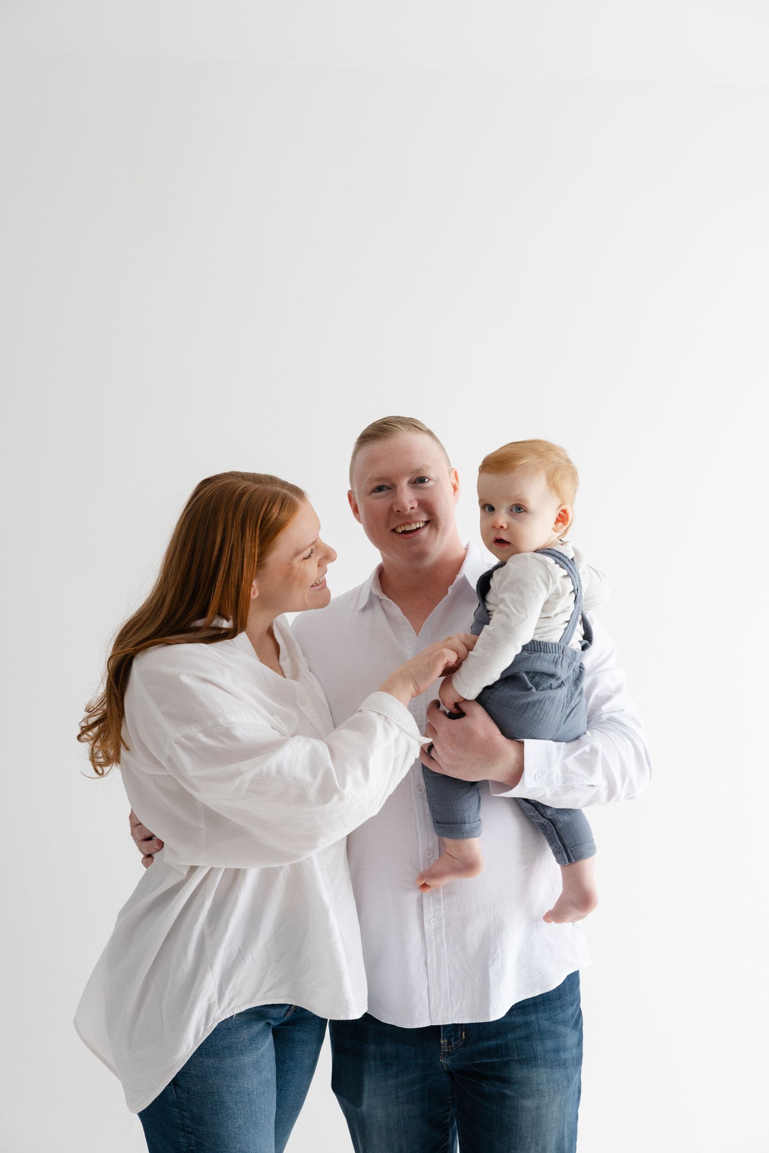 A family wearing white shirts and jeans poses together against a white backdrop in a series of playful photos.