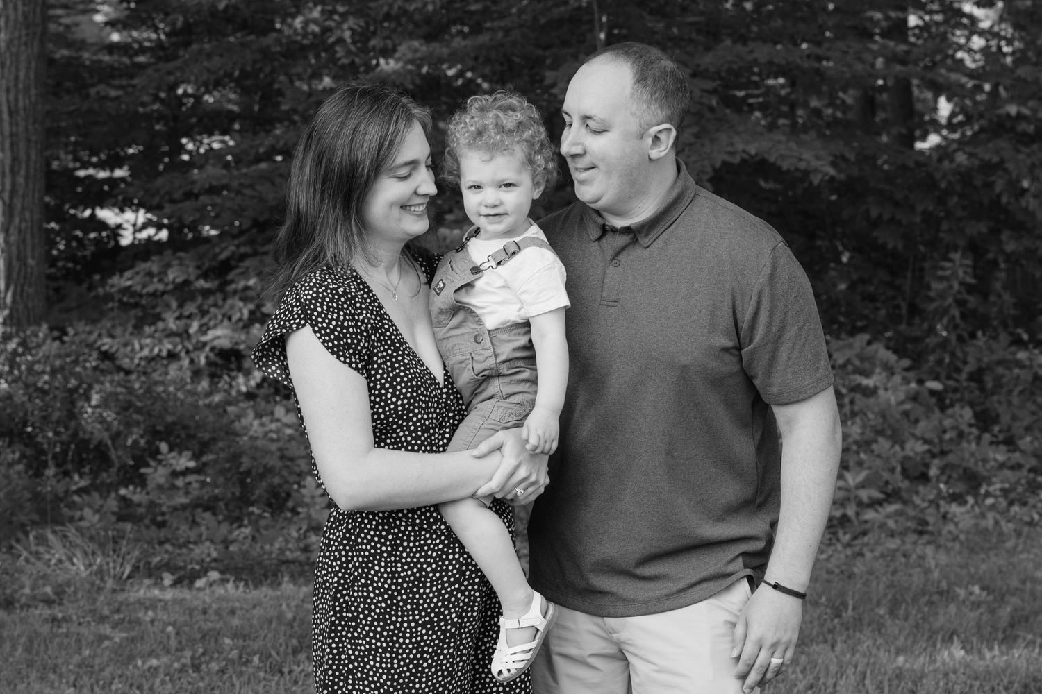 A family shares tender moments while posing outdoors in casual clothing for a black and white photo session.