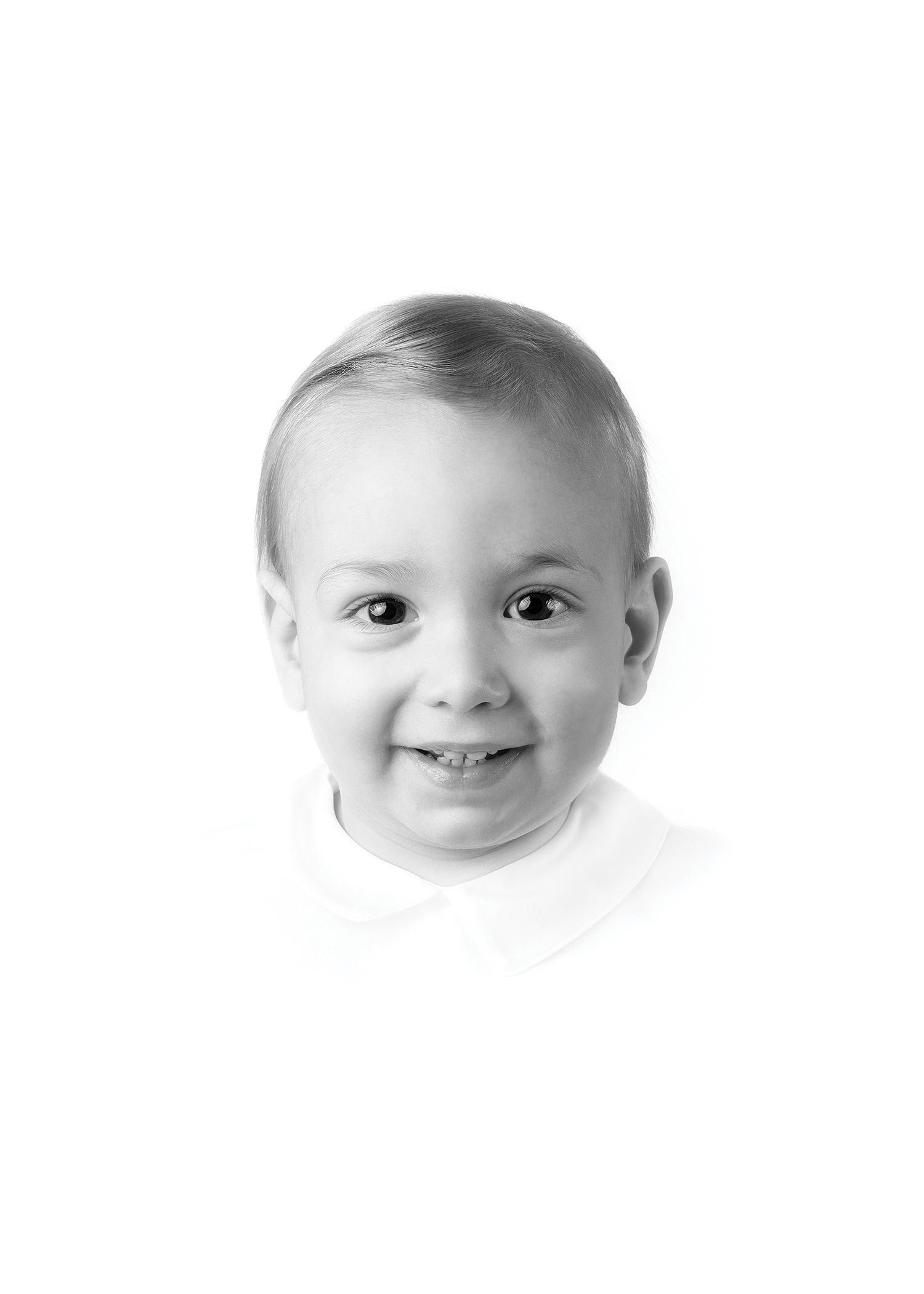 Black and white portrait photo of a smiling young toddler boy with short blonde hair wearing a white shirt.