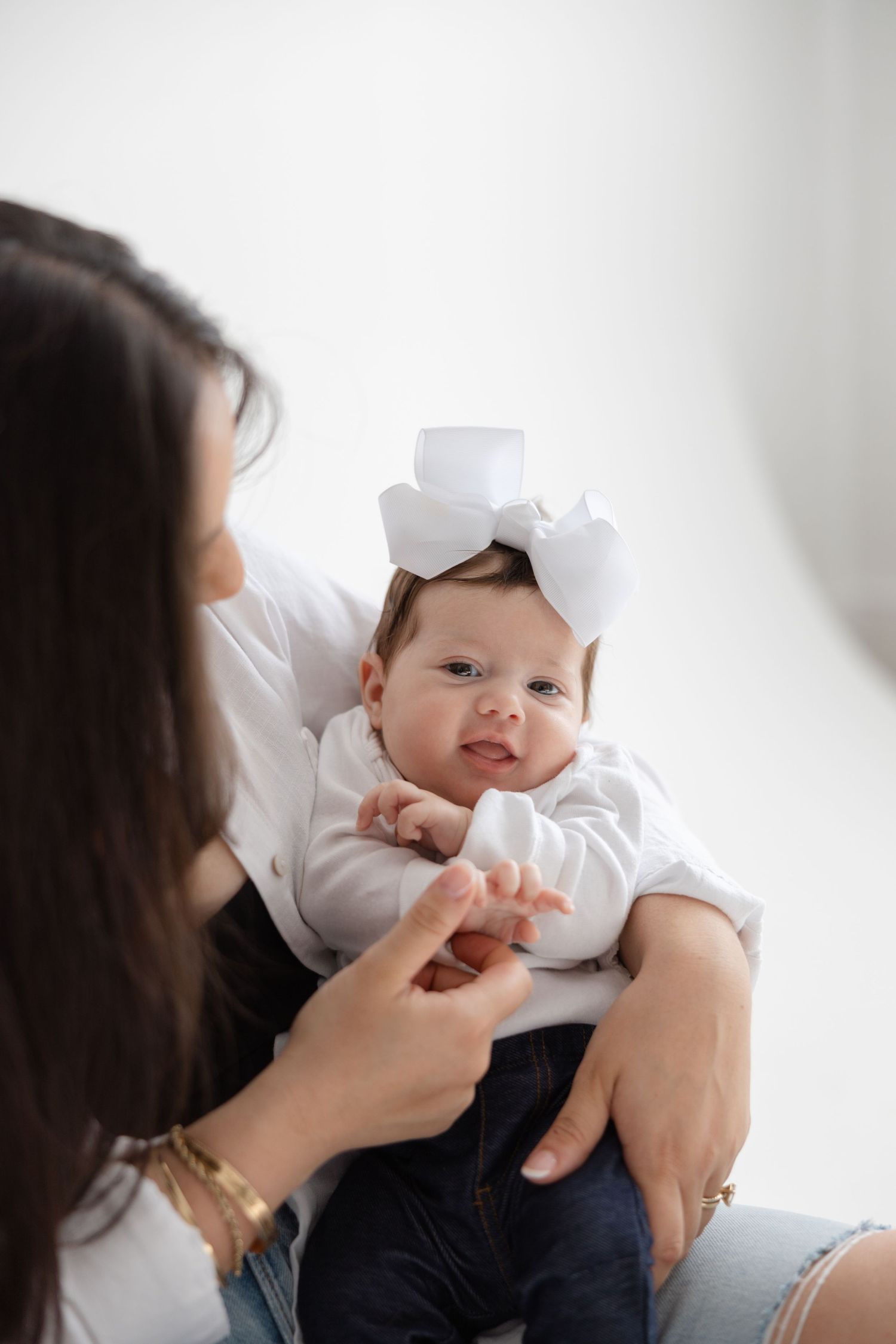 A baby wearing white clothing lies on someone's lap while interacting with their caregiver.