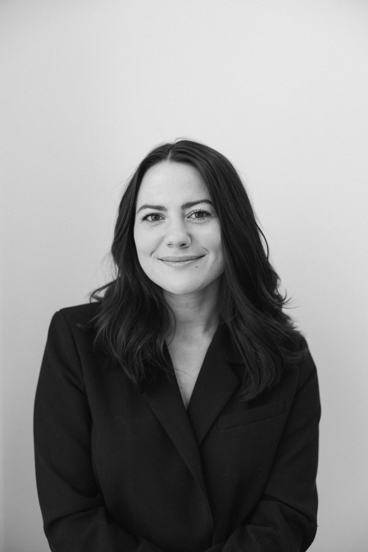 Professional black and white portrait of someone in a dark blazer smiling against a light background.