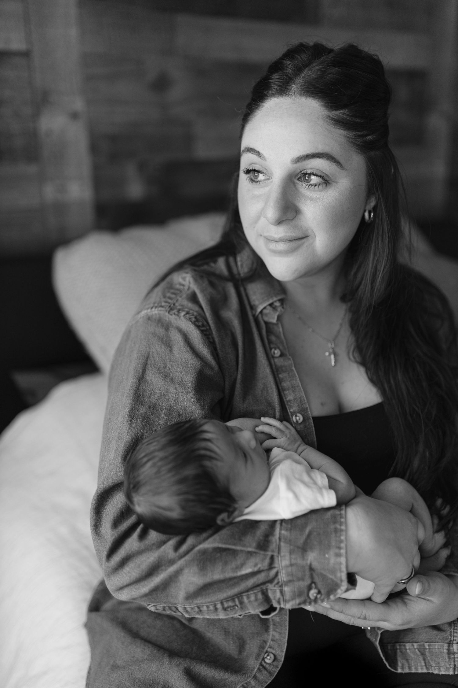 Black and white portrait of someone wearing denim jacket cradling a sleeping infant in a tender moment.