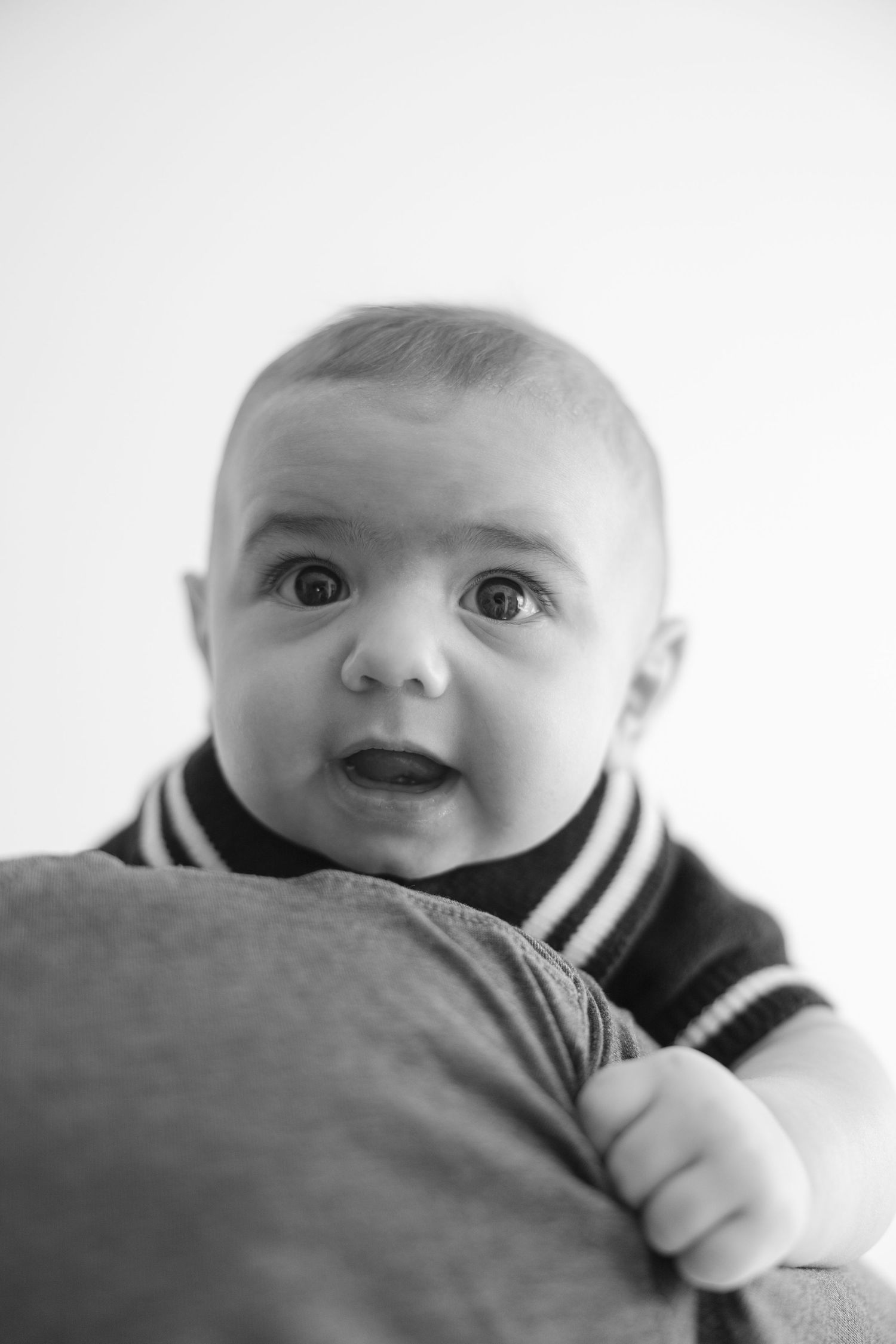 Black and white portrait photo of a small baby in a striped outfit gazing upward with an expressive look.