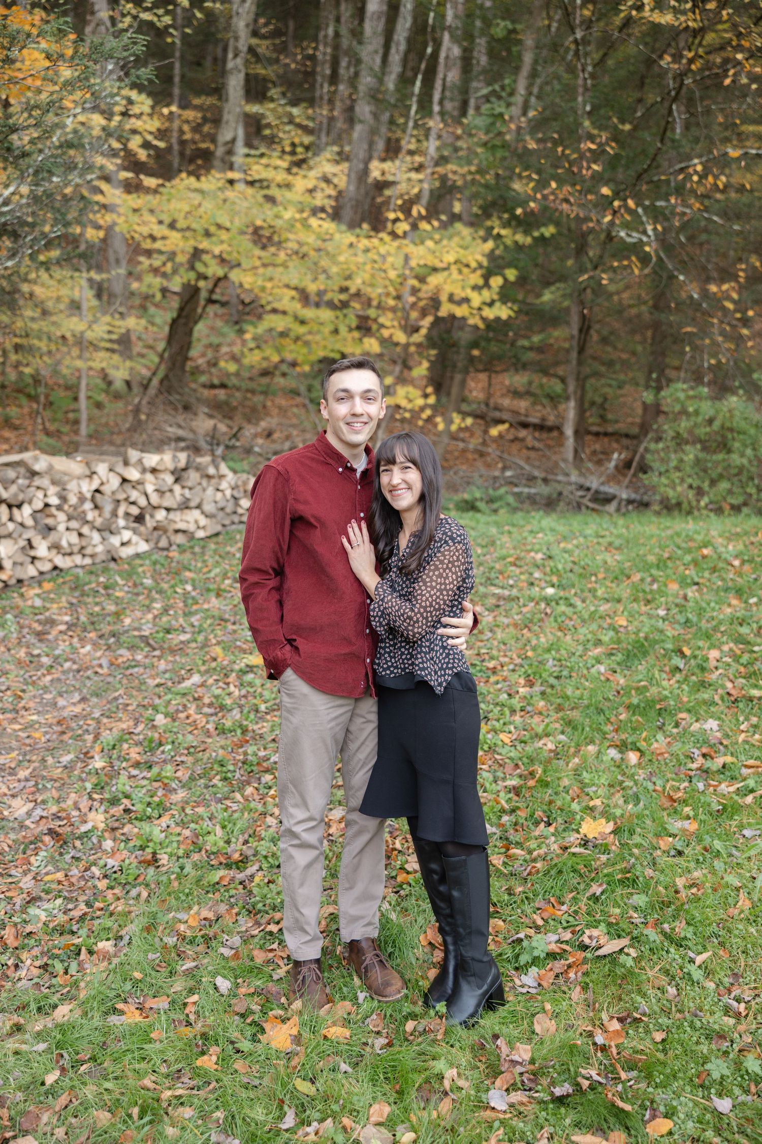 A couple stands together on fallen autumn leaves in a wooded area during a fall photo session.