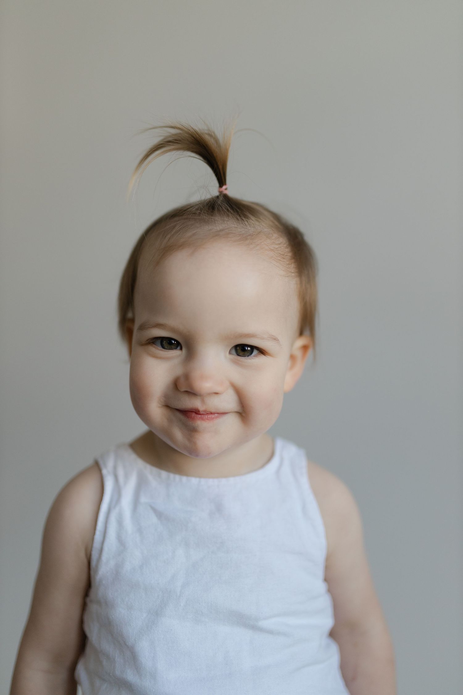 A baby in a white sleeveless dress makes various cheerful expressions against a gray background.