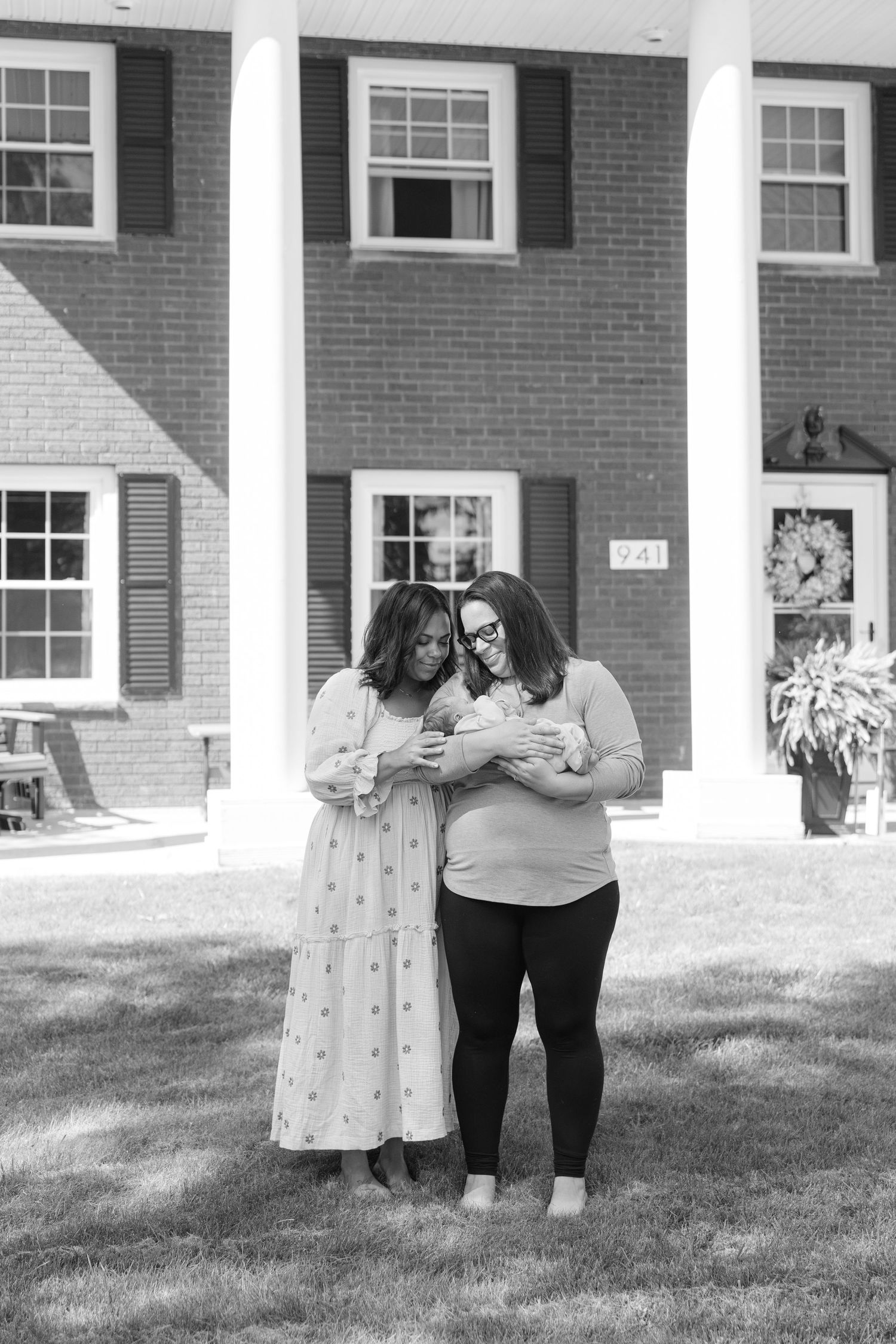 Two friends share a sweet moment together while standing on the lawn in front of a brick house with white columns.
