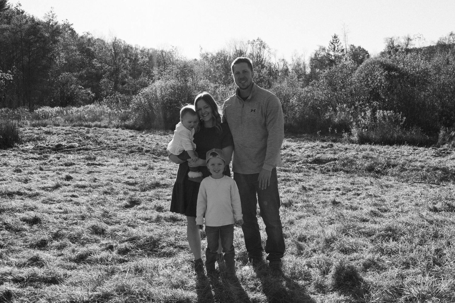 A series of black and white family moments captured outdoors in a field with natural lighting.