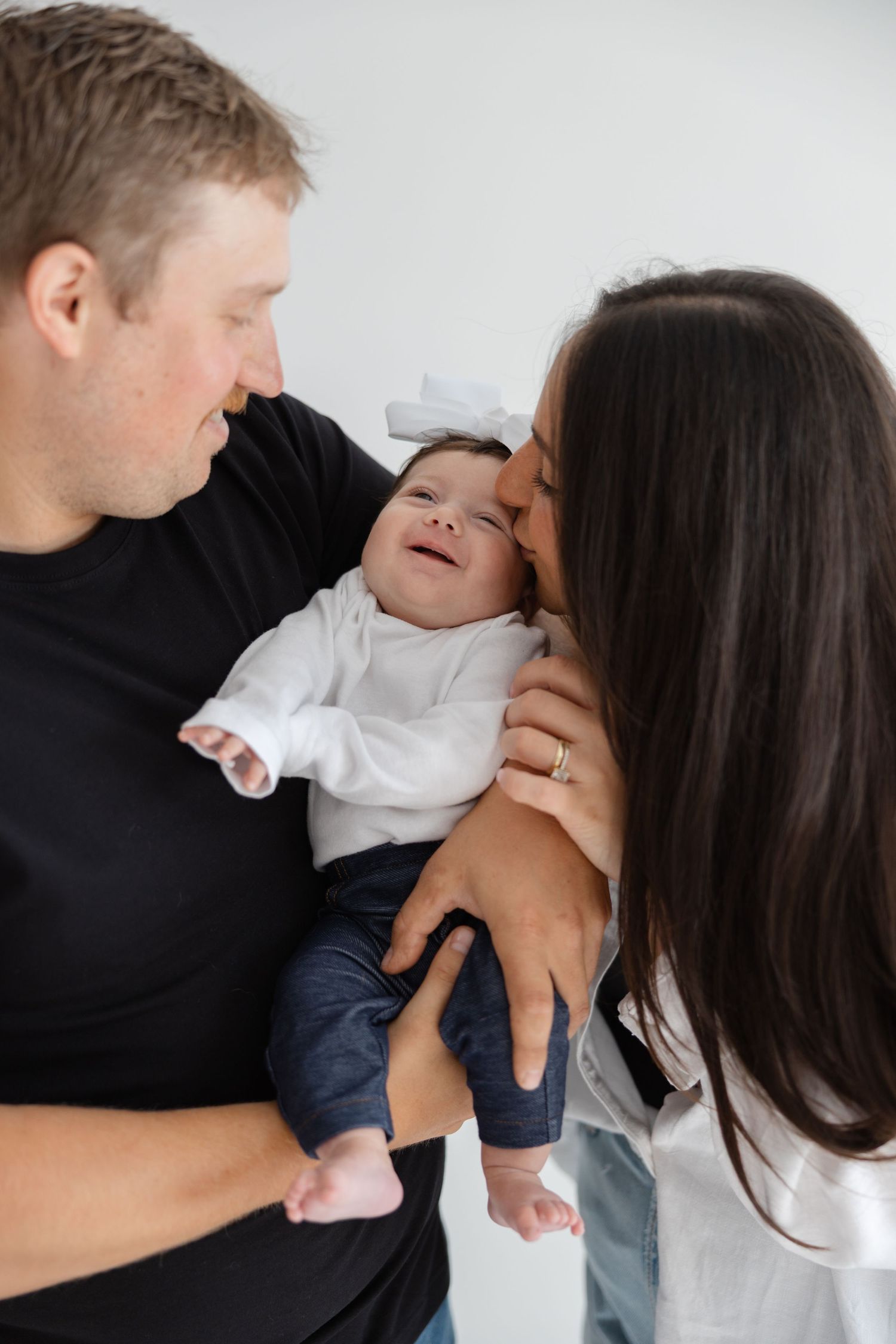 Close family sharing a tender moment together as they huddle around their smiling baby in white and navy outfit.