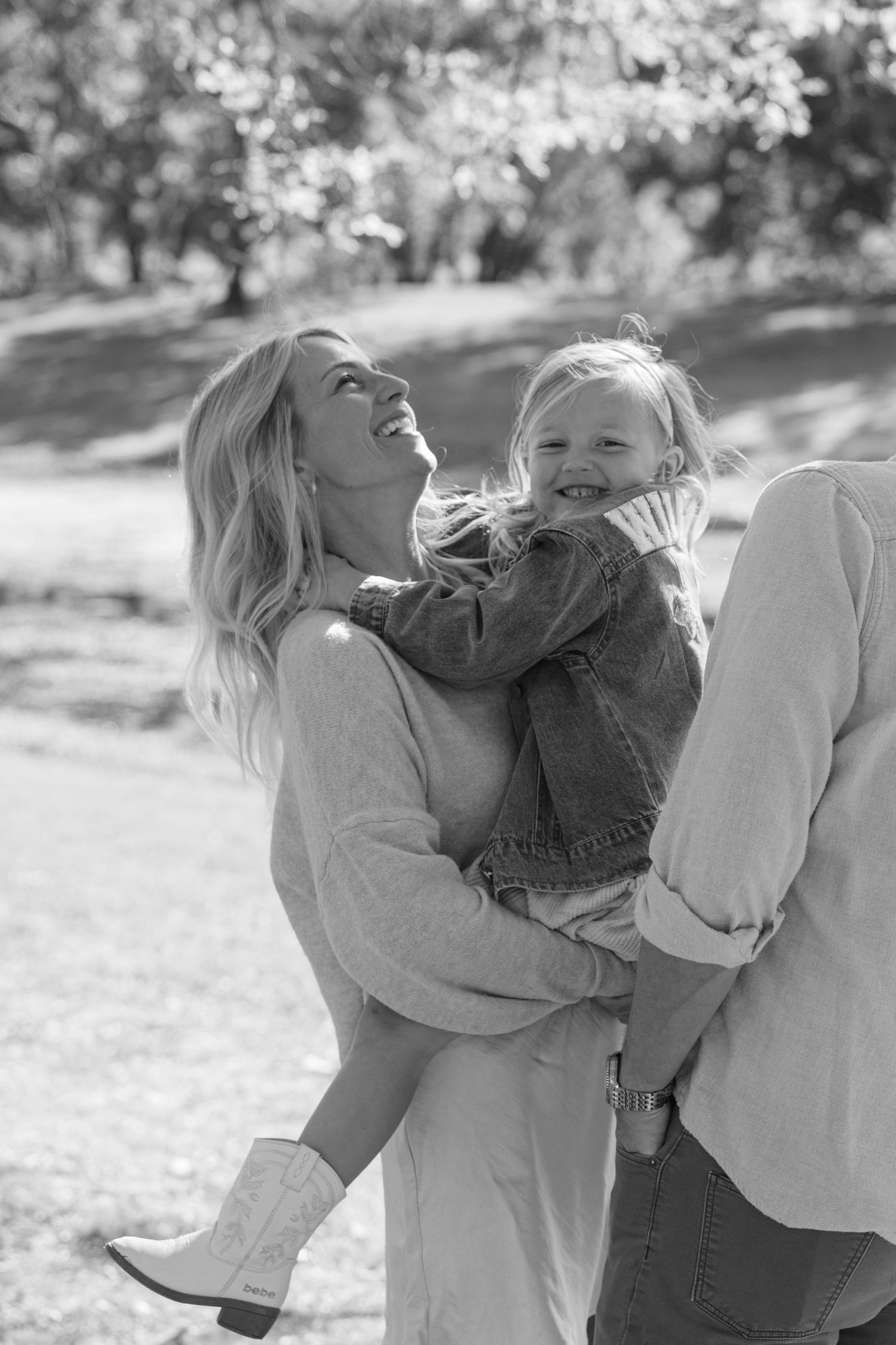 A series of candid black and white photos showing playful family moments outdoors in natural lighting.
