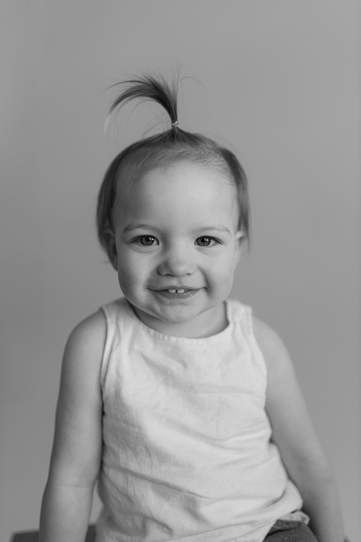 A series of photos showing a happy baby in a white tank top making different facial expressions on a gray backdrop.