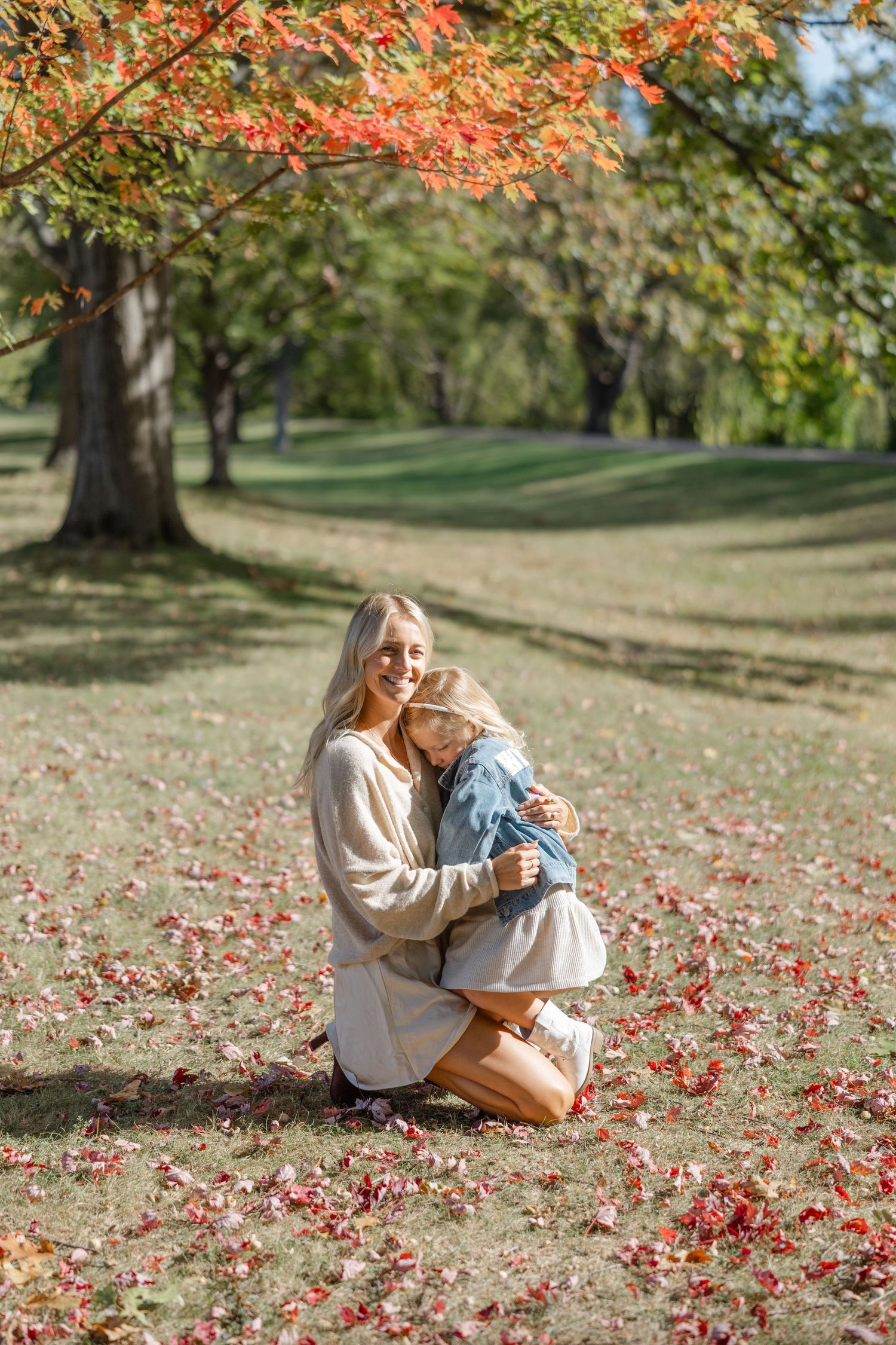 A tender autumn moment under red maple leaves as two people embrace on fallen foliage in a peaceful park setting.