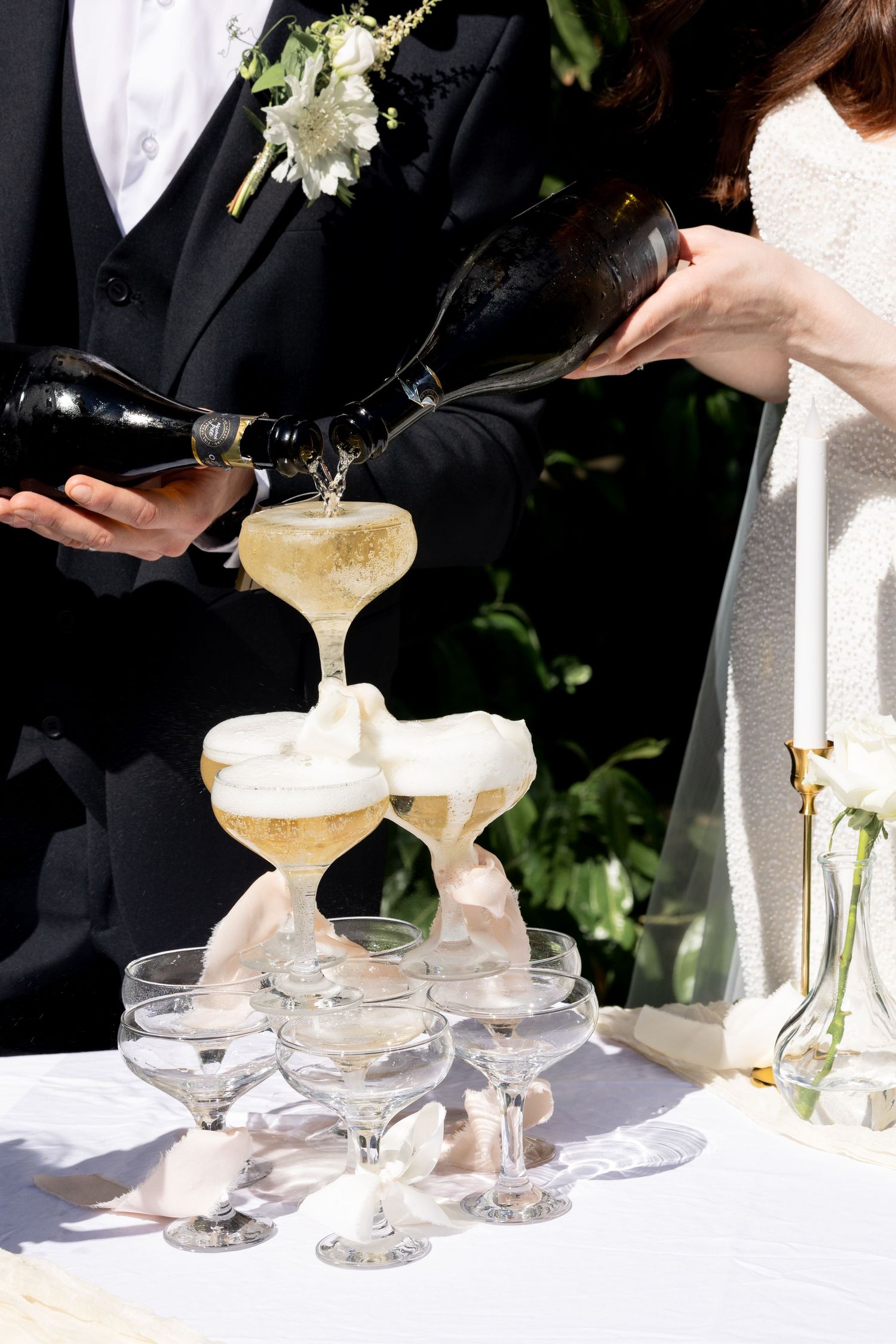 Champagne tower. The couple pouring champagne into a tower of coupe glasses. Natural documentary wedding photography.