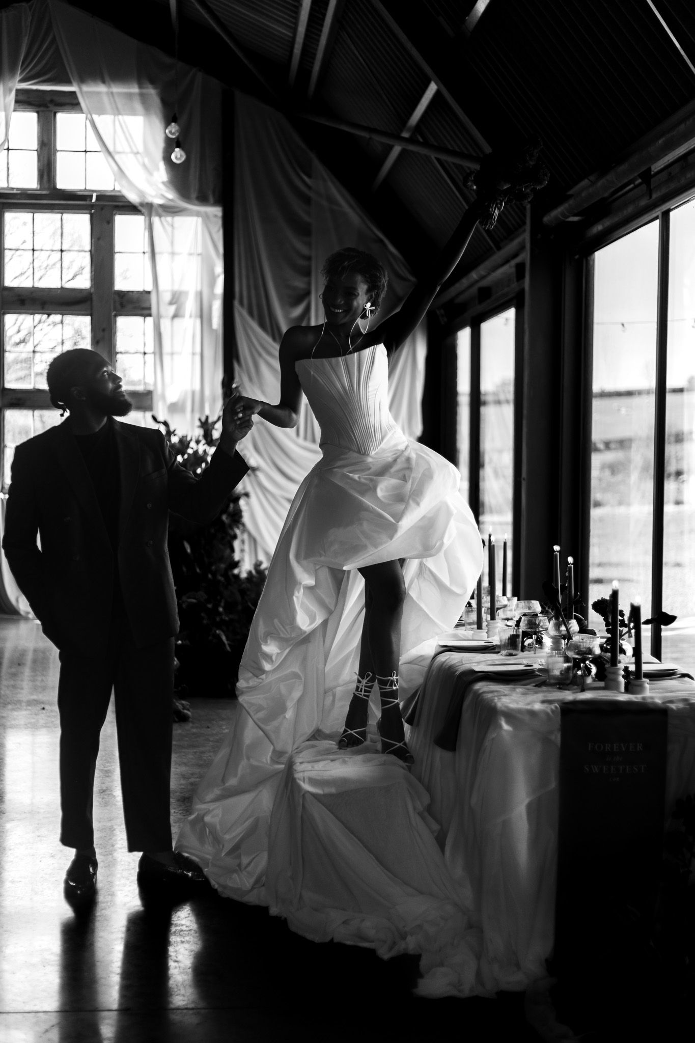 Couple hand in hand laughing as bride dances on the wedding breakfast chair