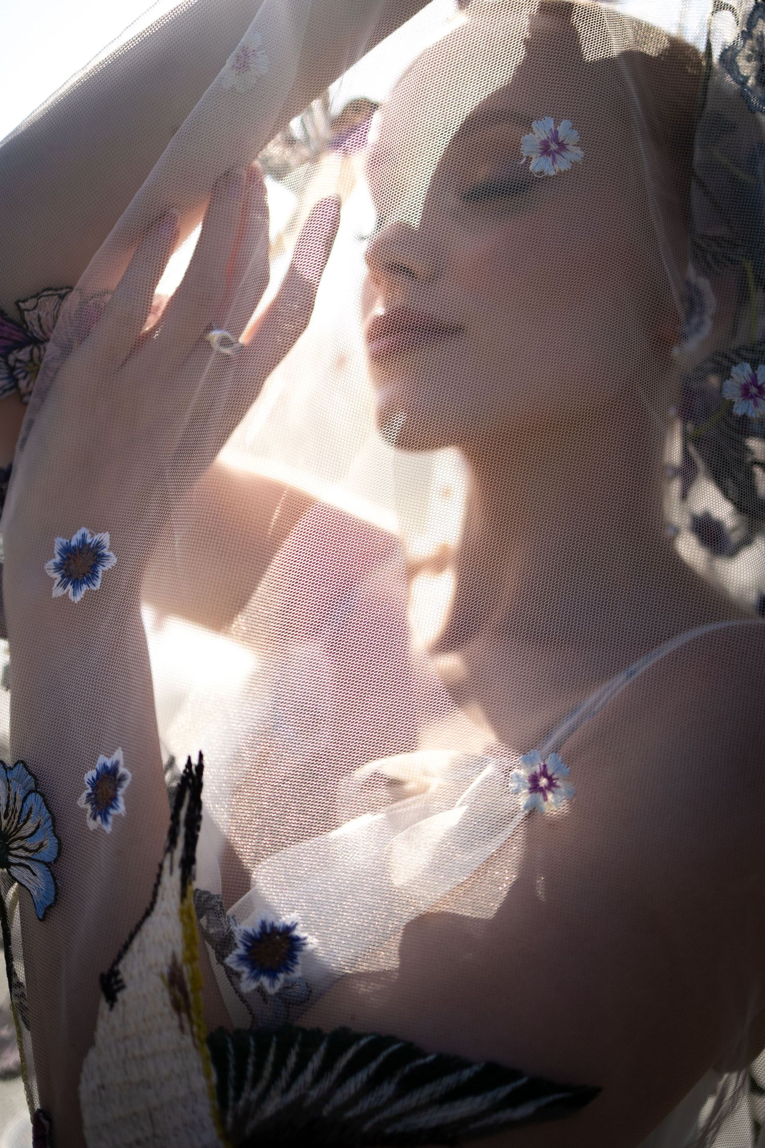 Elegant bride with a detailed veil with floral embroidery. Eyes closed and smiling in the sun