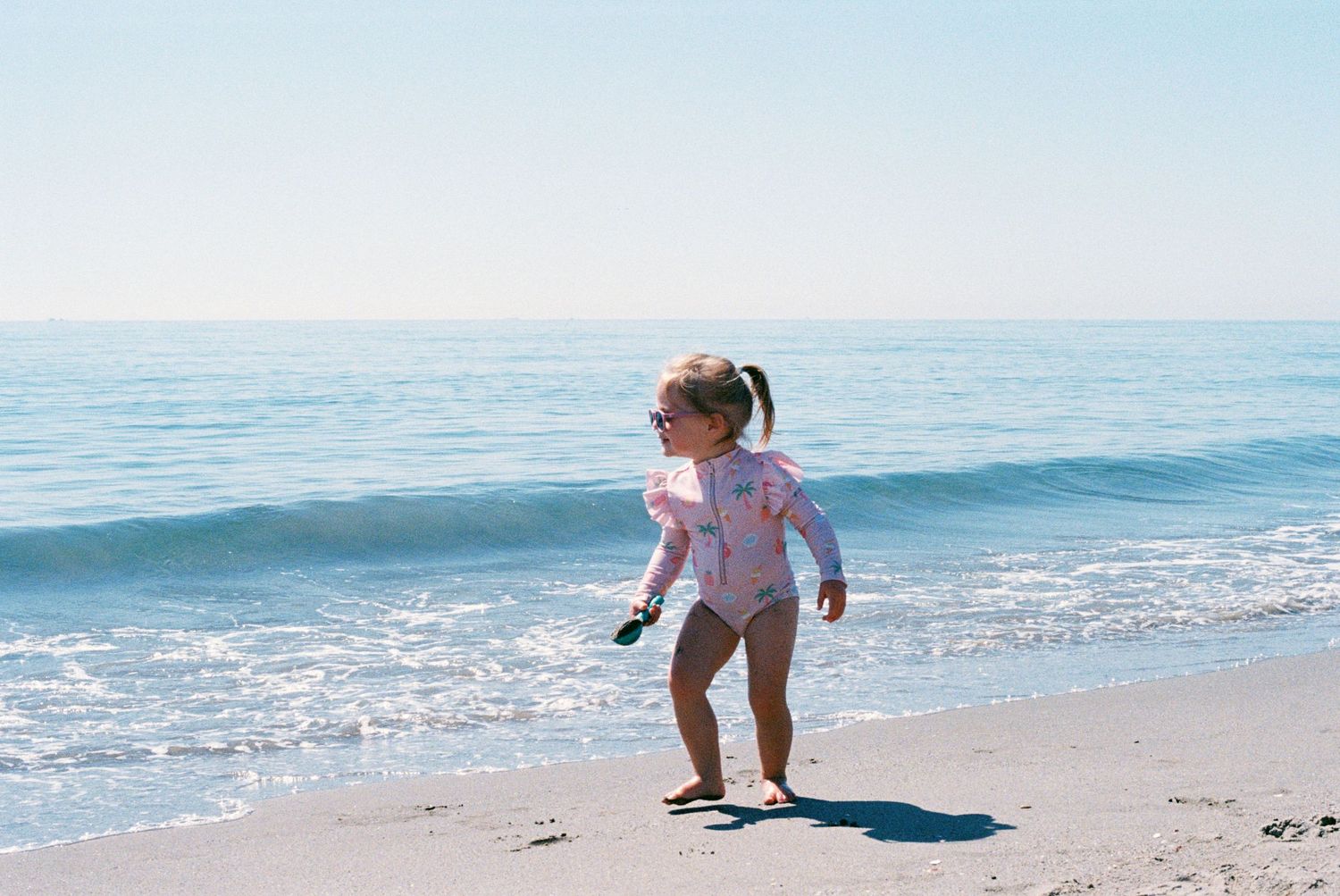 Family photograph at the beach of toddler looking out at the sea. Taken on 35mm film. Documentary photography. Film photography.