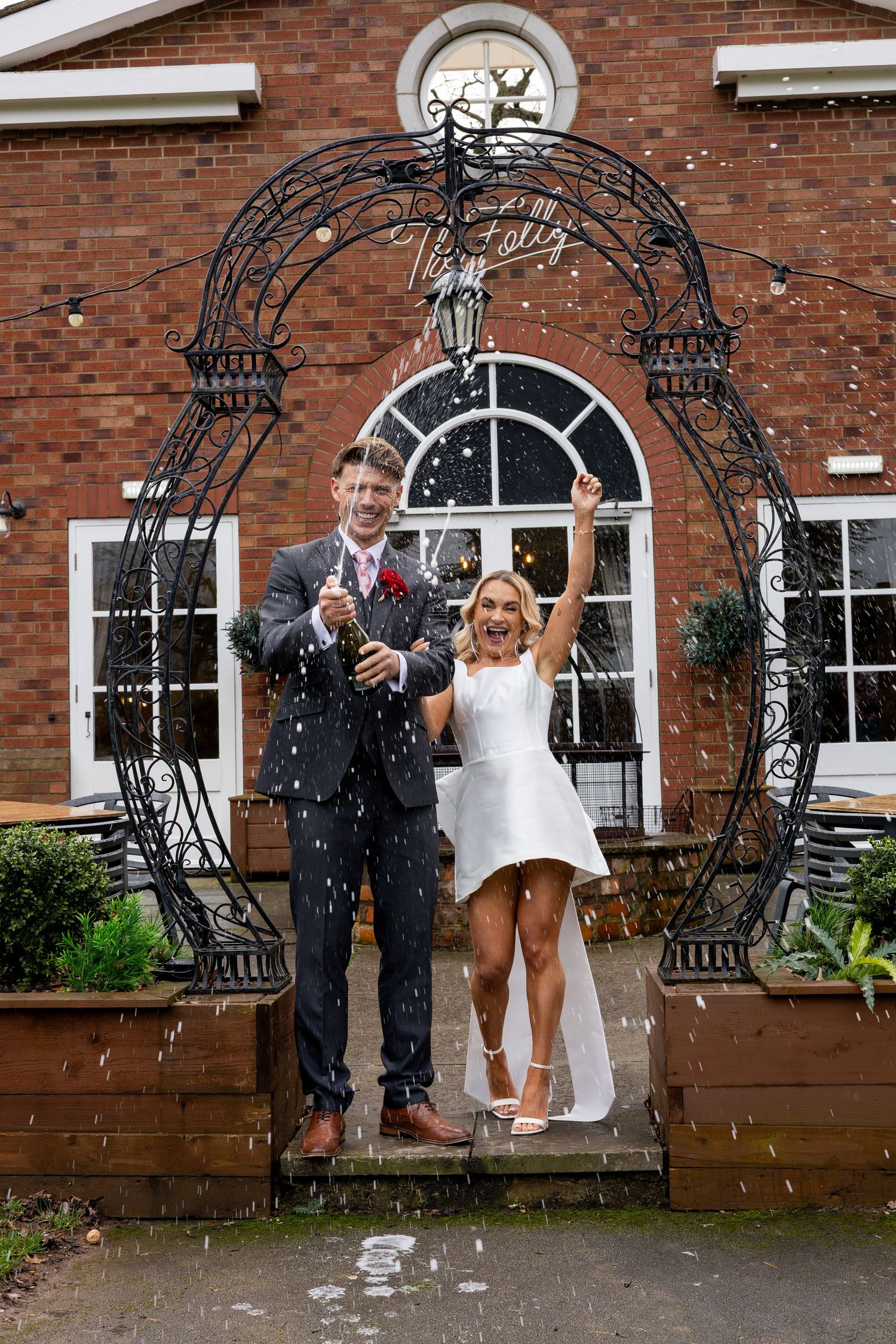 Bride and groom laughing during their champagne spray at The Folly Farmhouse Mackworth wedding venue
