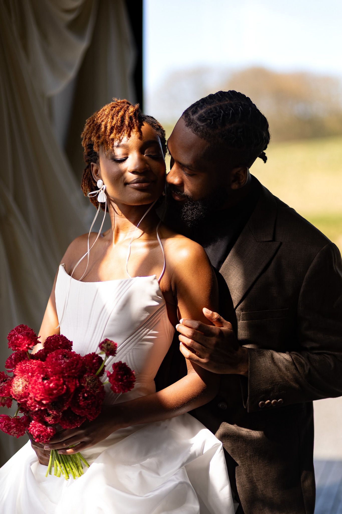 Golden hour glow. Couple in love in the soft sunlight with deep red bouquet