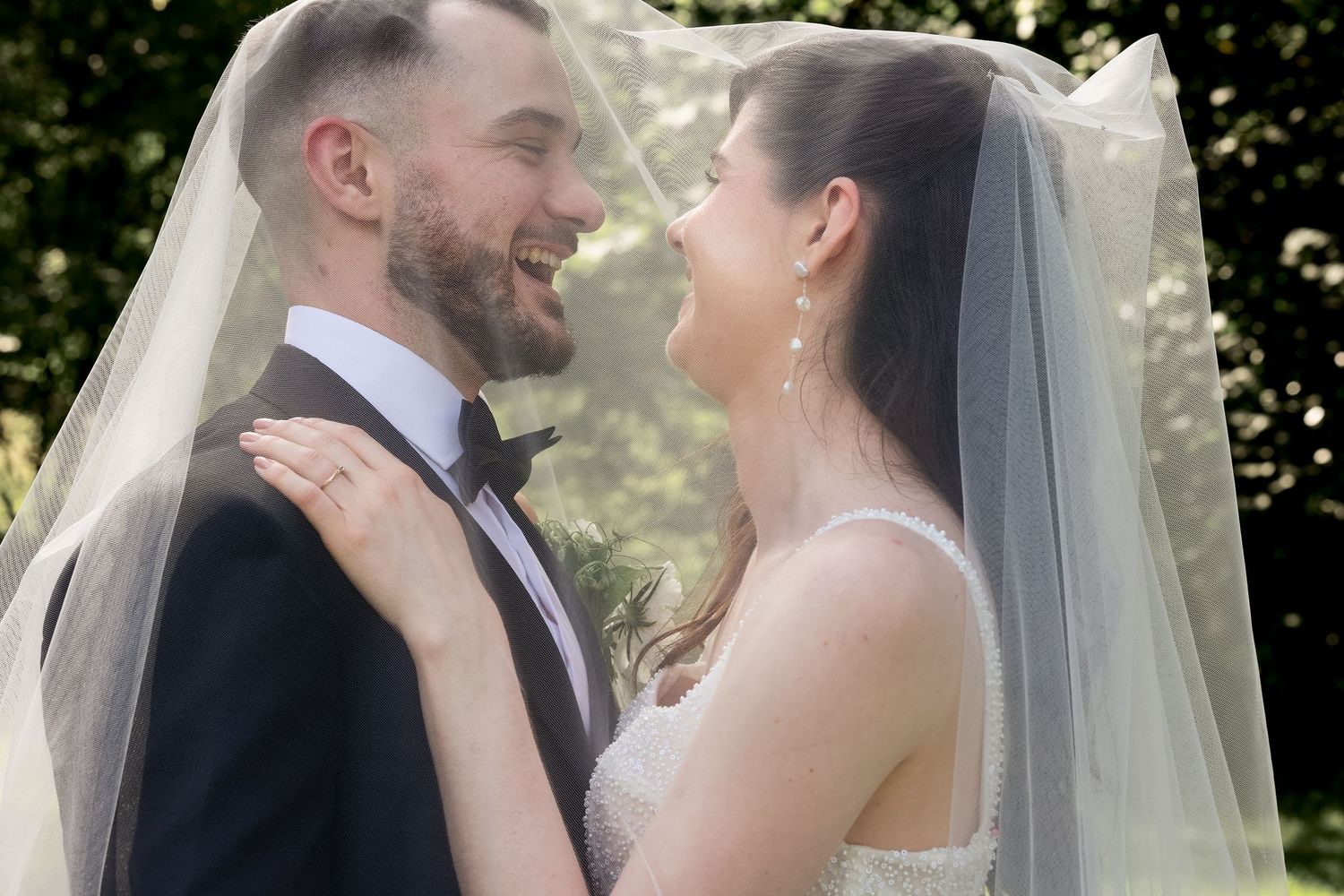 A couple laughing underneath the brides veil on their wedding day. Natural documentary wedding photography.
