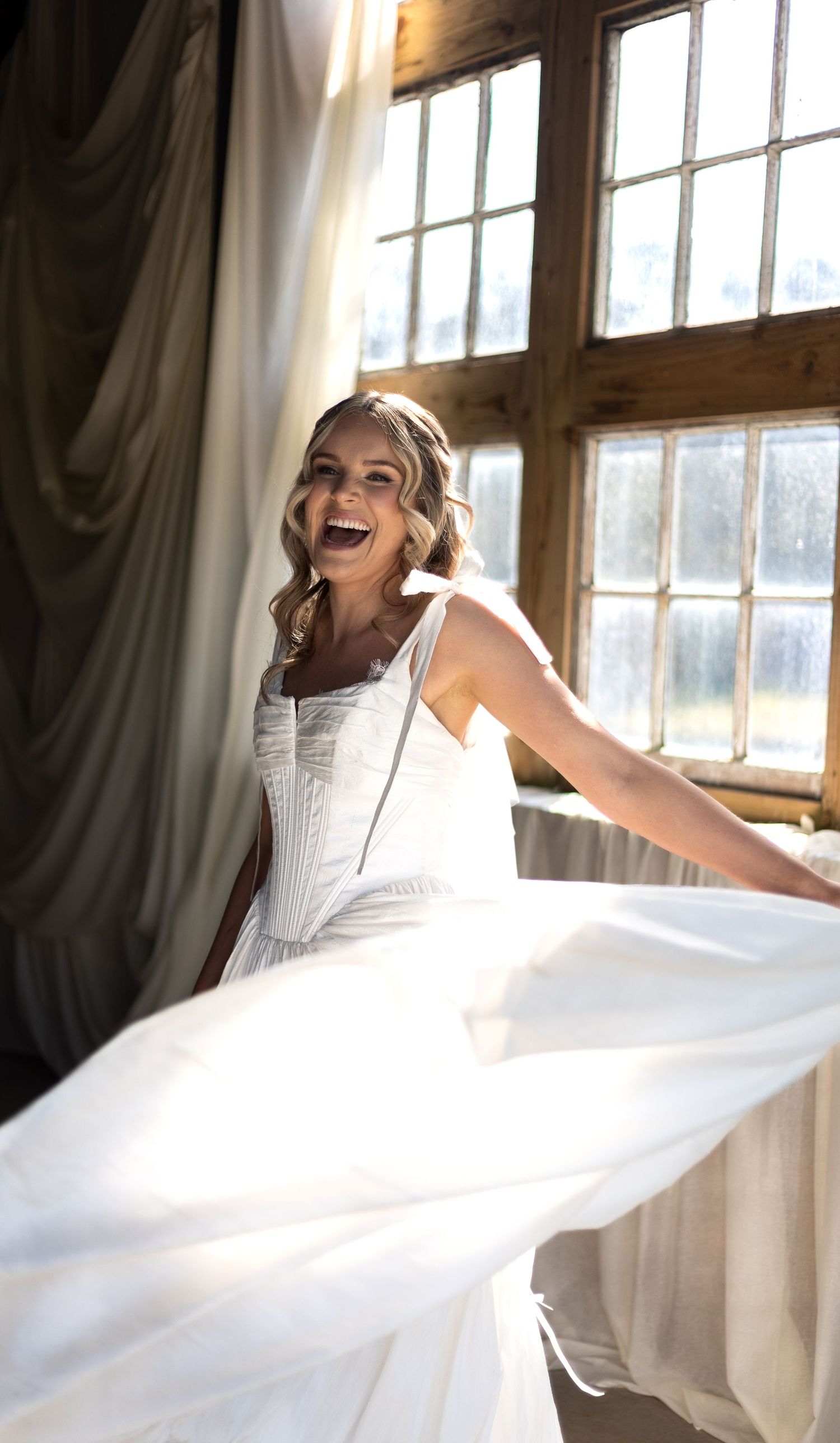 Beautiful bride in golden hour spinning her dress around whilst laughing full of joy. Natural documentary wedding photography