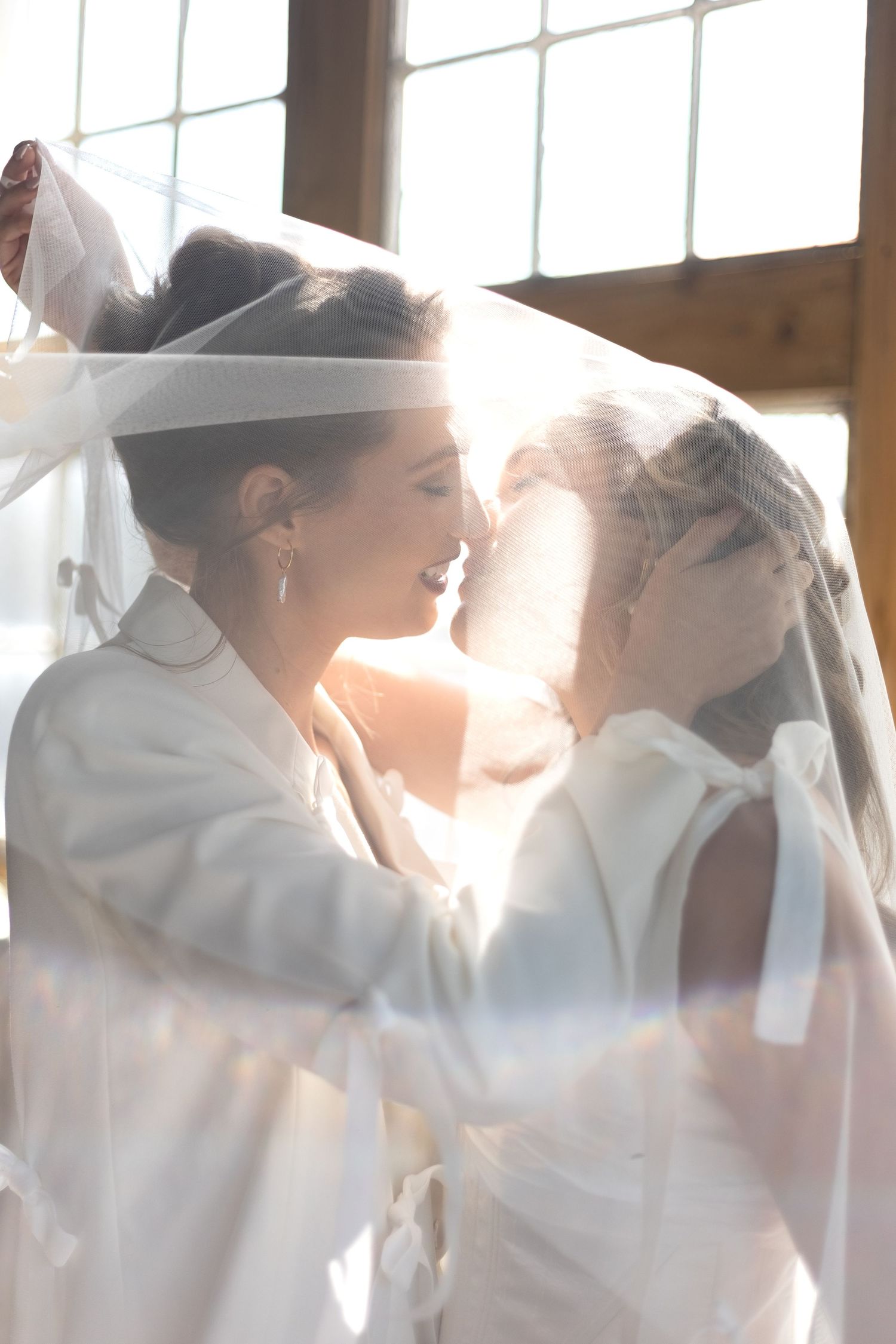 Female couple having a romantic kiss behind the veil. Natural documentary wedding photography