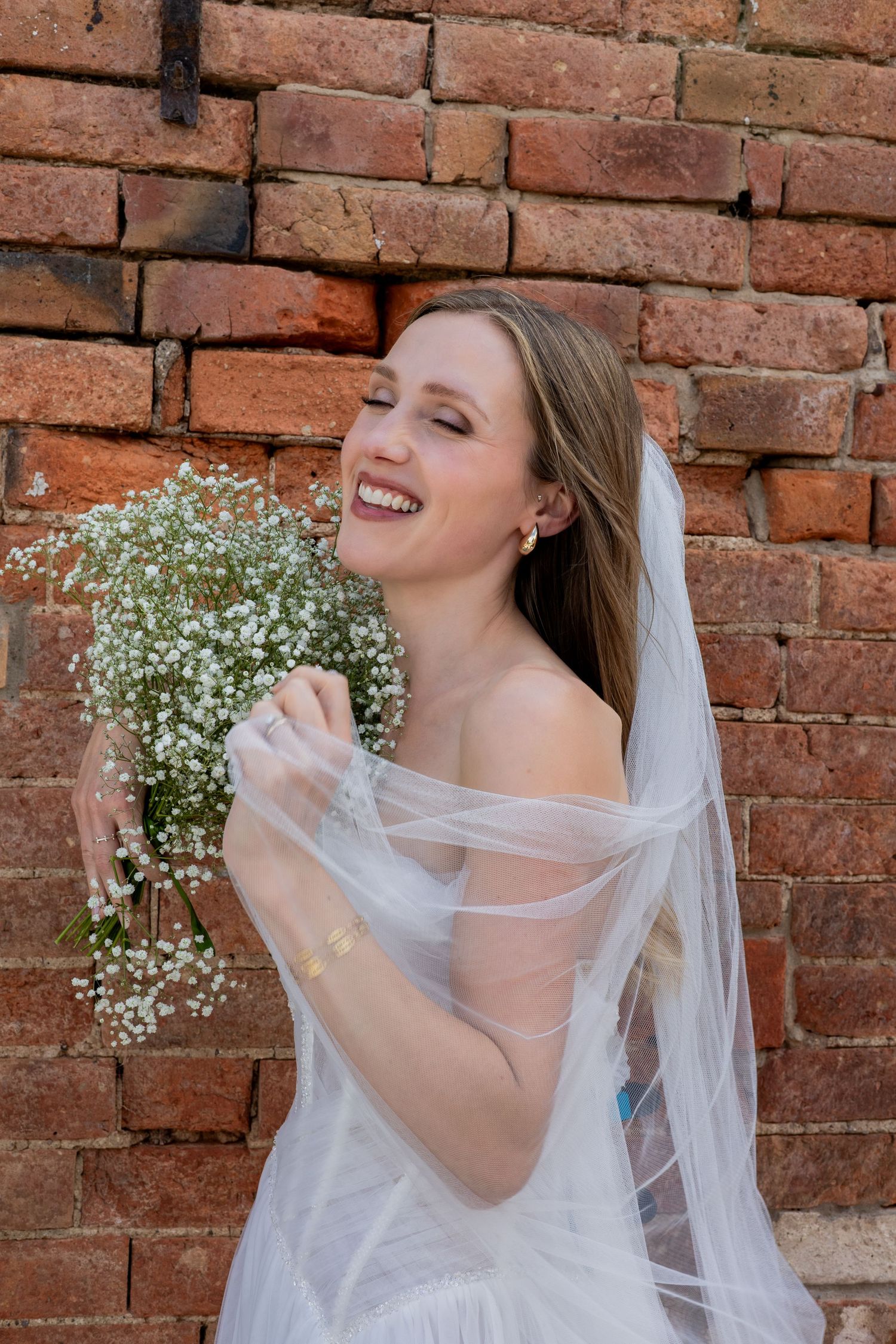 A joyful laughing bride holding her bouquet outside The Fable Yard in the Midlands.