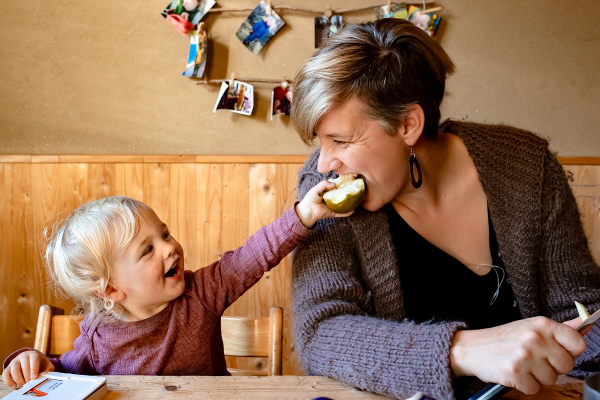 Kleinkind füttert lachend seine Mutter am Küchentisch – ungestellter Familienmoment bei der Familienfotografie Bad Oldesloe