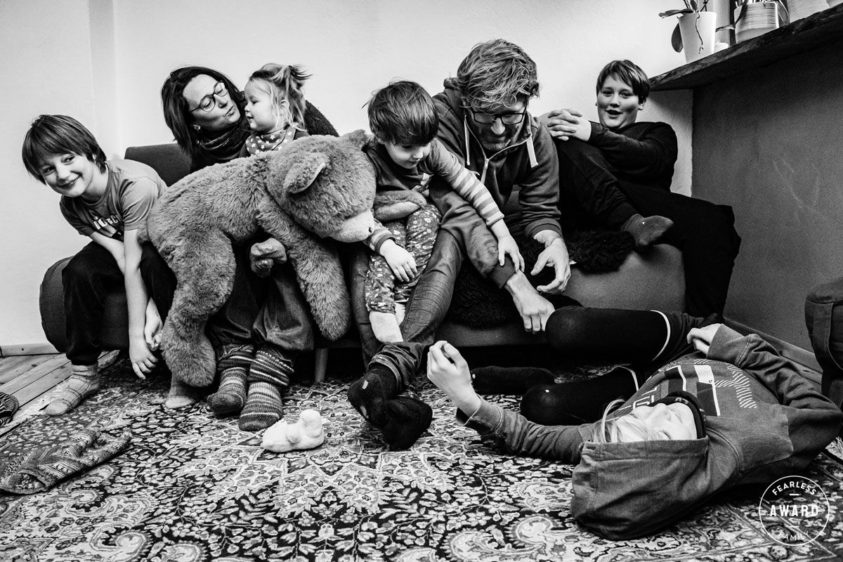 Große Familie tobt lachend zusammen auf dem Sofa mit riesigem Teddybär – Fearless Award, dokumentarische Familienfotografie Lübeck
