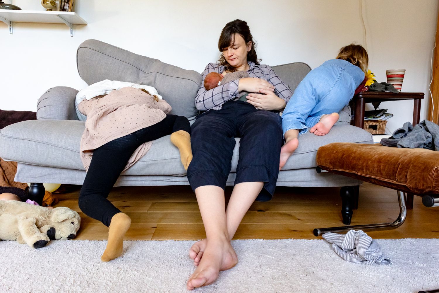 Mutter stillt Neugeborenes auf dem Sofa, Geschwisterkinder toben daneben – echtes Wochenbett-Chaos – Wochenbettfotografie Lübeck
