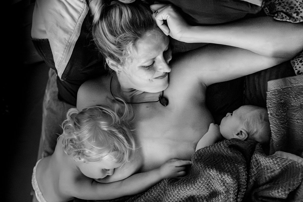 Mutter liegt erschöpft und glücklich mit Neugeborenem und Geschwisterkind nach der Hausgeburt – Wochenbettfotografie Lübeck, Sylvia Fischer