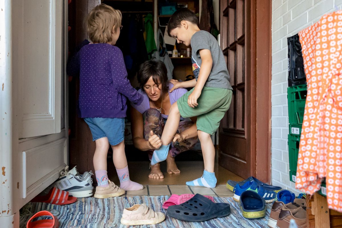 Mama kniet im Flur und hilft ihren zwei Söhnen beim Schuhe anziehen – authentische Familienfotografie im Alltag, Lübeck