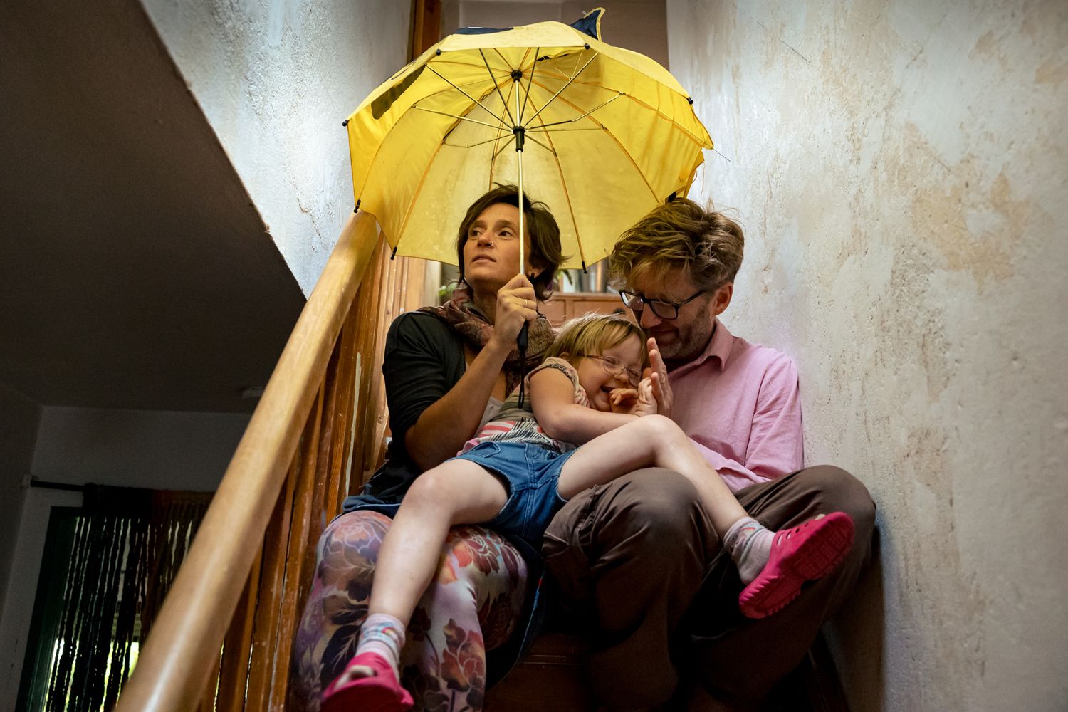 Familie sitzt mit gelbem Regenschirm auf der Treppe – skurriler, echter Familienmoment bei der Familienfotografie Lübeck