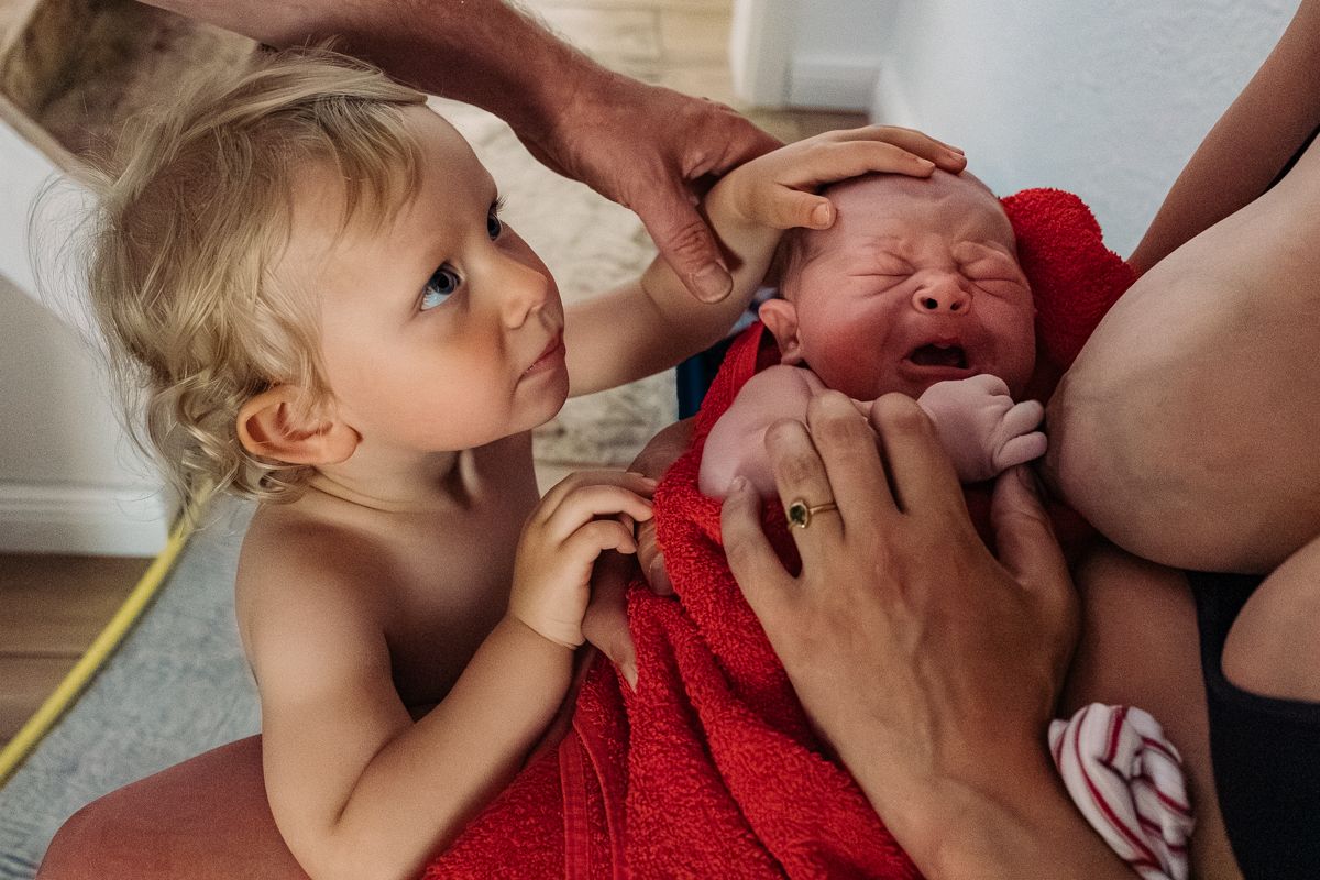 Geschwisterkind berührt zärtlich das Neugeborene kurz nach der Geburt – Geburtsreportage Lübeck, Sylvia Fischer Fotografie