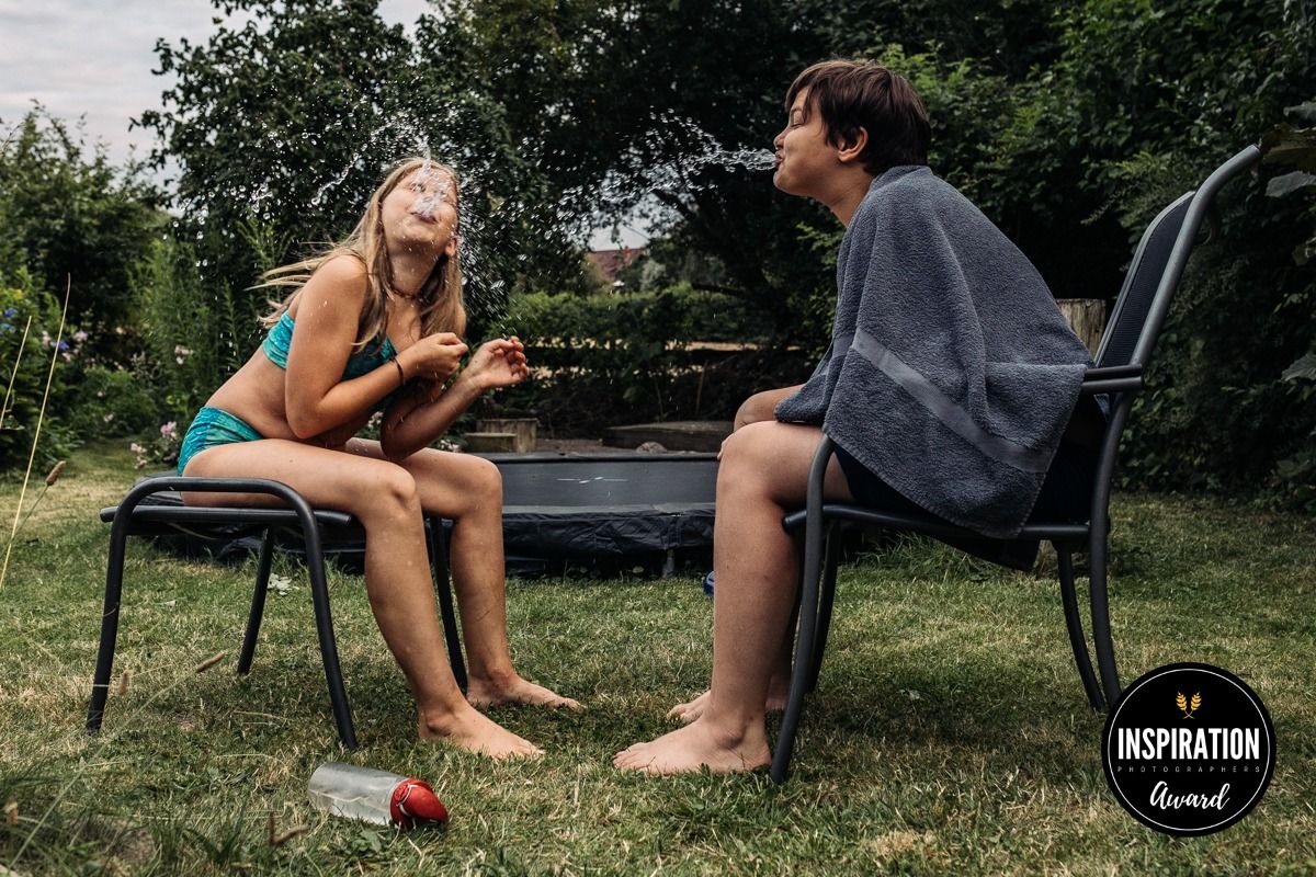 Zwei Kinder spritzen sich gegenseitig Wasser ins Gesicht im Garten – preisgekrönte dokumentarische Familienfotografie, Lübeck