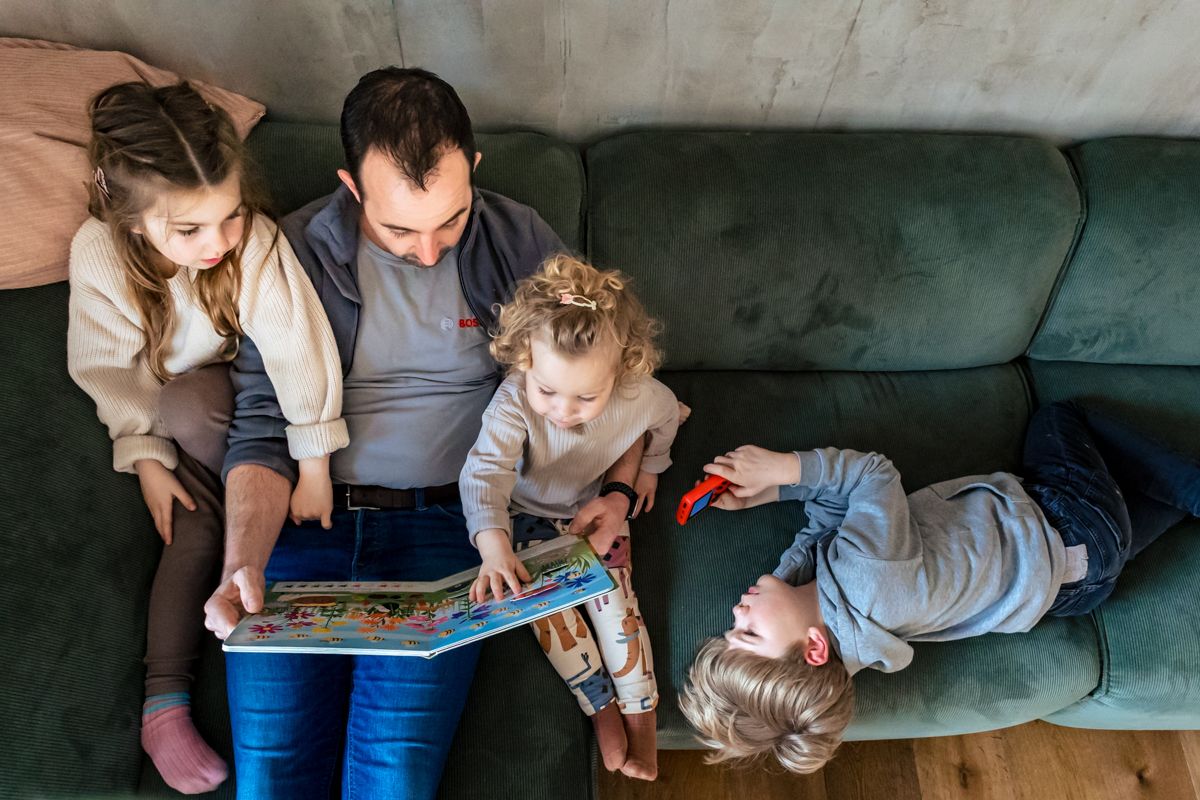 Vater liest drei Kindern auf dem Sofa vor – echter Familienalltag bei der Familienreportage Lübeck