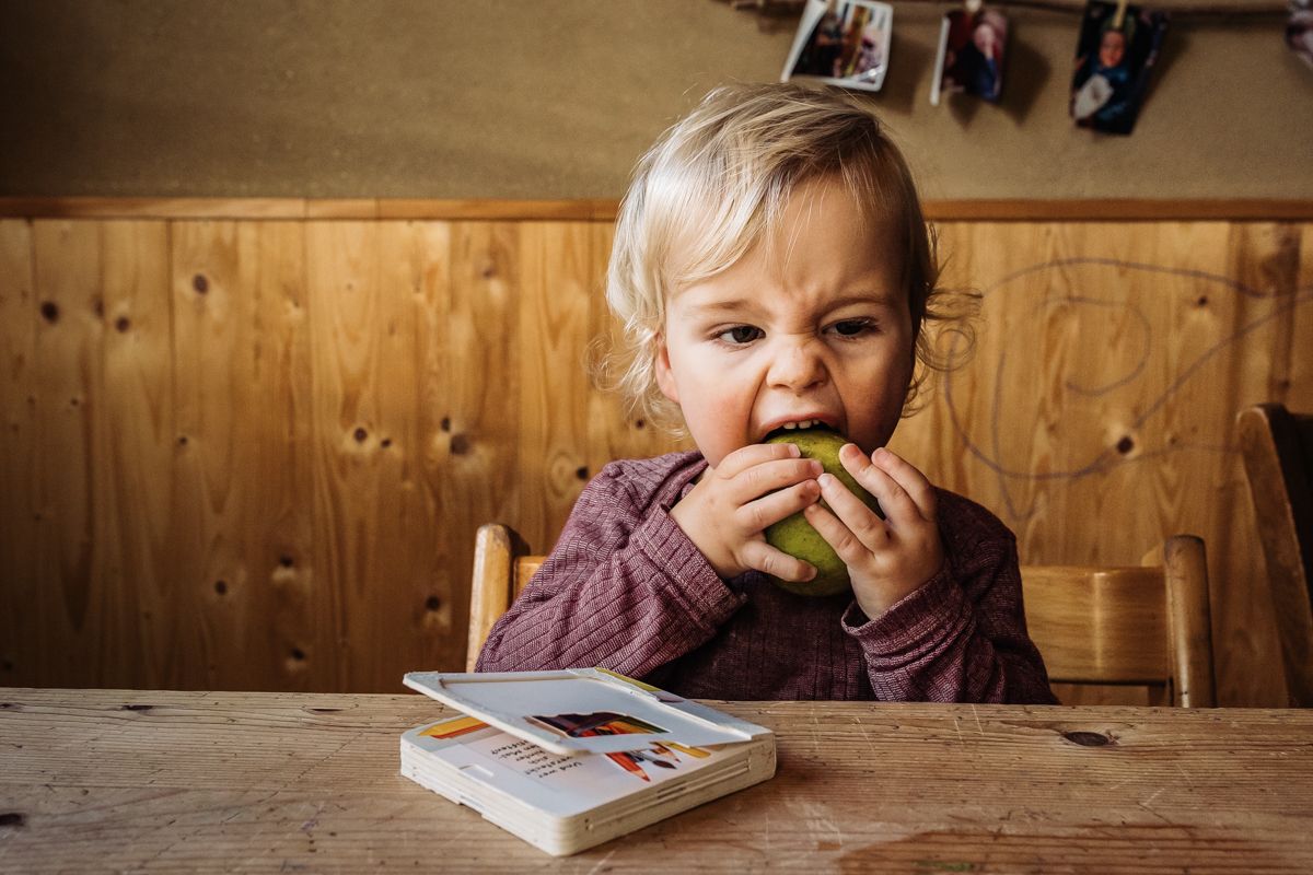 Kleinkind beißt konzentriert in einen Apfel am Küchentisch – authentisches Familienshooting Lübeck, Sylvia Fischer Fotografie