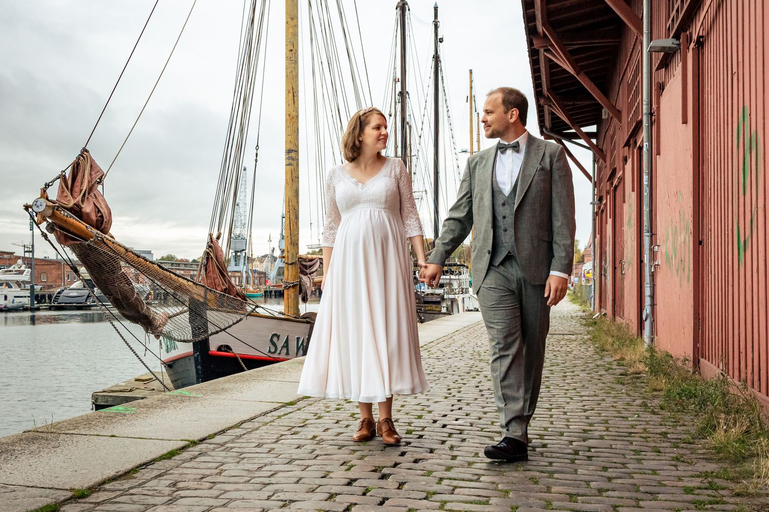Brautpaar spaziert Hand in Hand am historischen Hafen Lübeck – natürliche Hochzeitsfotografie Lübeck, Sylvia Fischer Fotografie