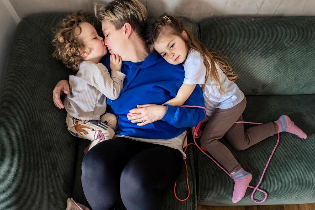 Zwei Kinder kuscheln sich von beiden Seiten an ihre Mutter auf dem Sofa – natürliche Familienfotografie Lübeck