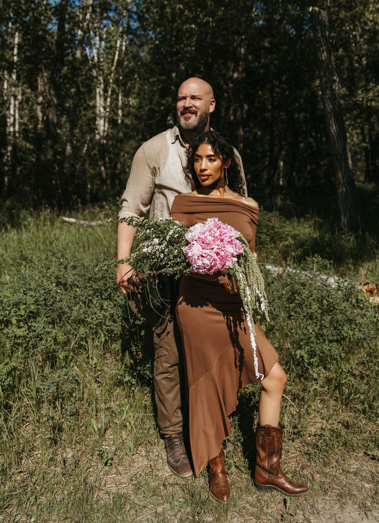 Two people embrace in a romantic outdoor photo session with rustic brown and pink color tones against a forest backdrop.