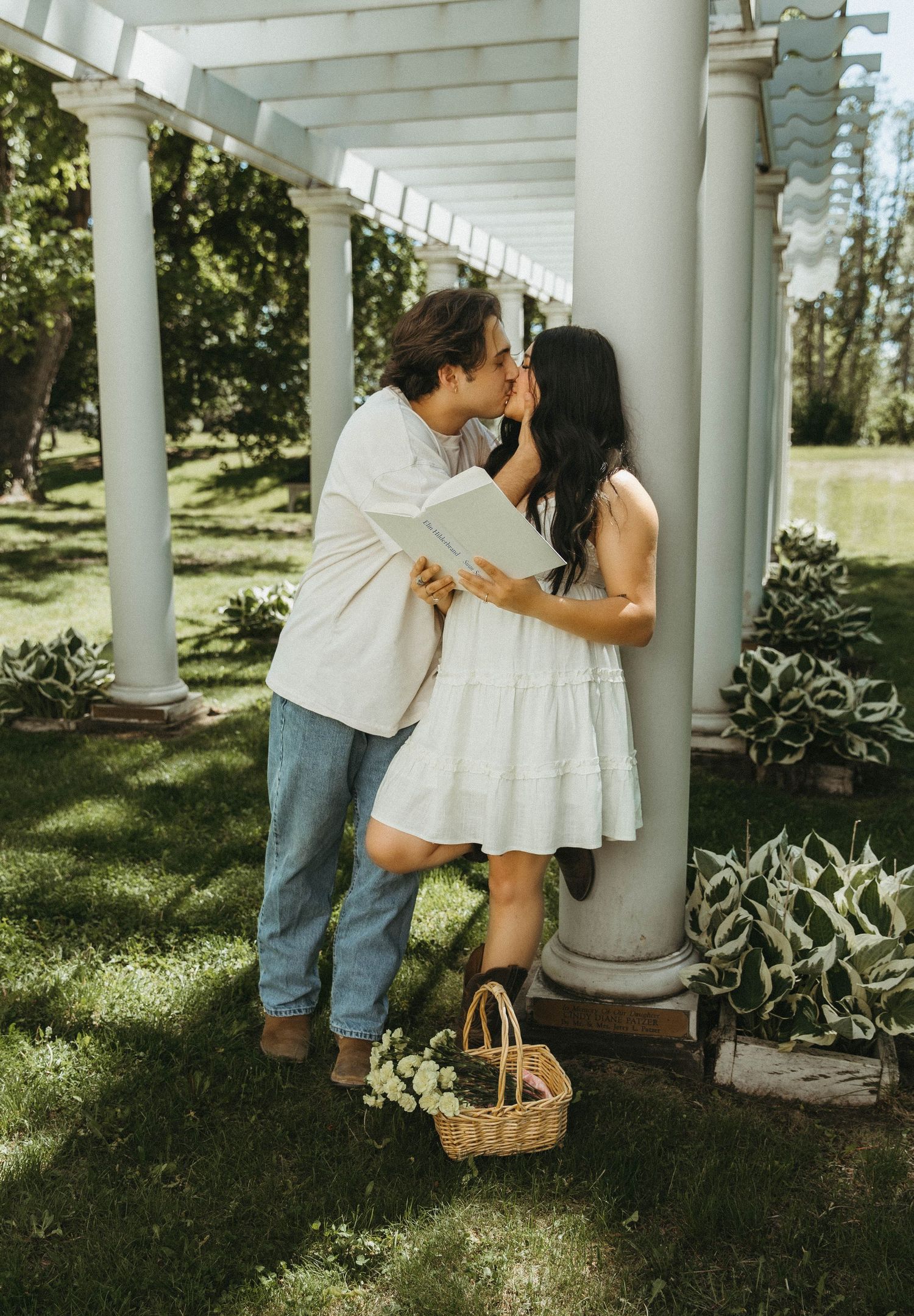 Romantic couple sharing a sweet moment under a white pergola in a lush garden setting.
