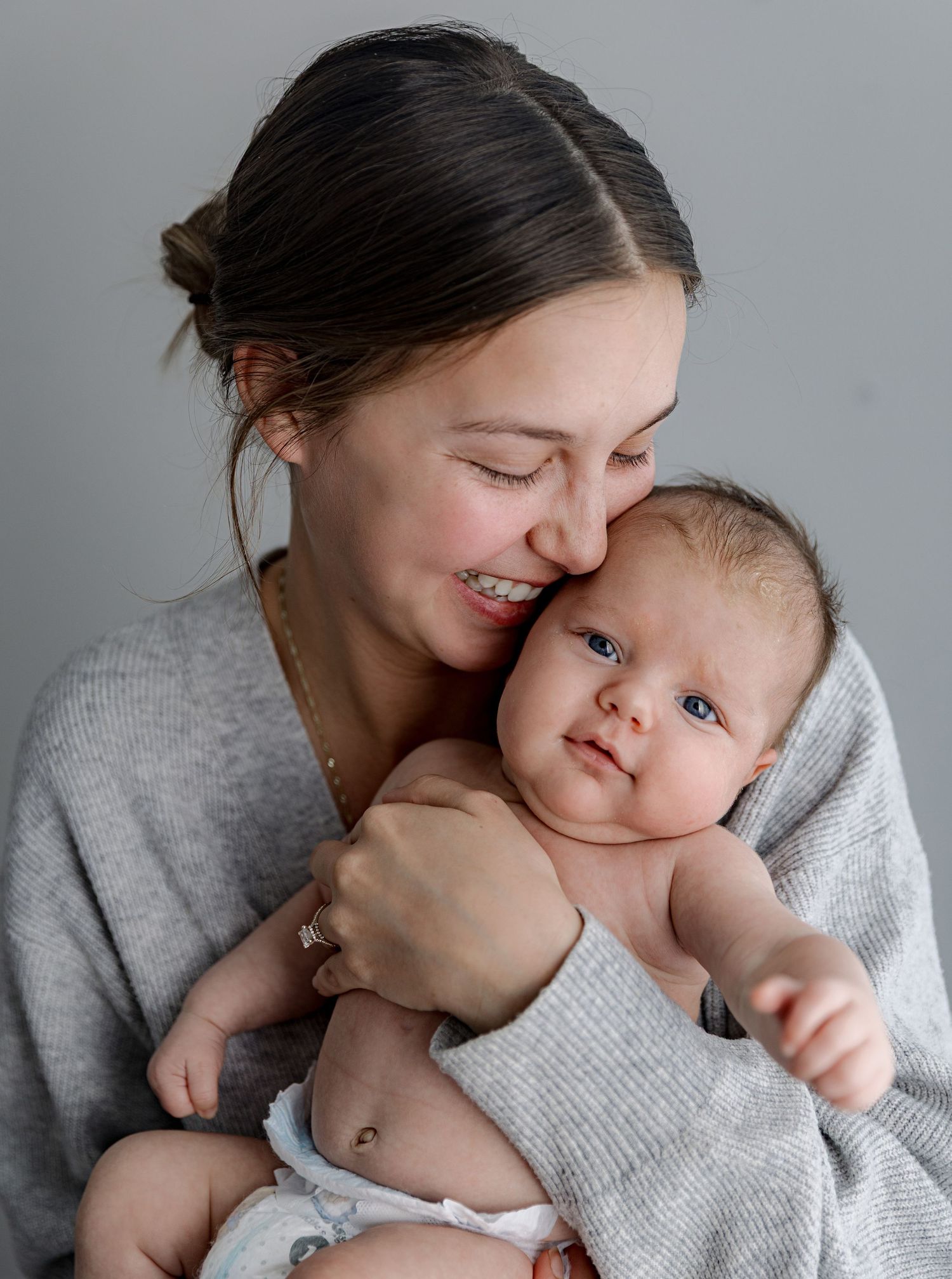 Mother in grey sweater sharing affectionate moments with baby in multiple candid shots.