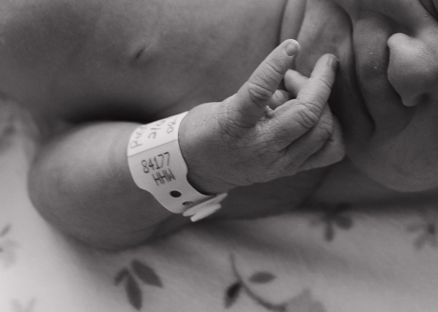 Tiny newborn baby foot with hospital identification bracelet in black and white photograph.