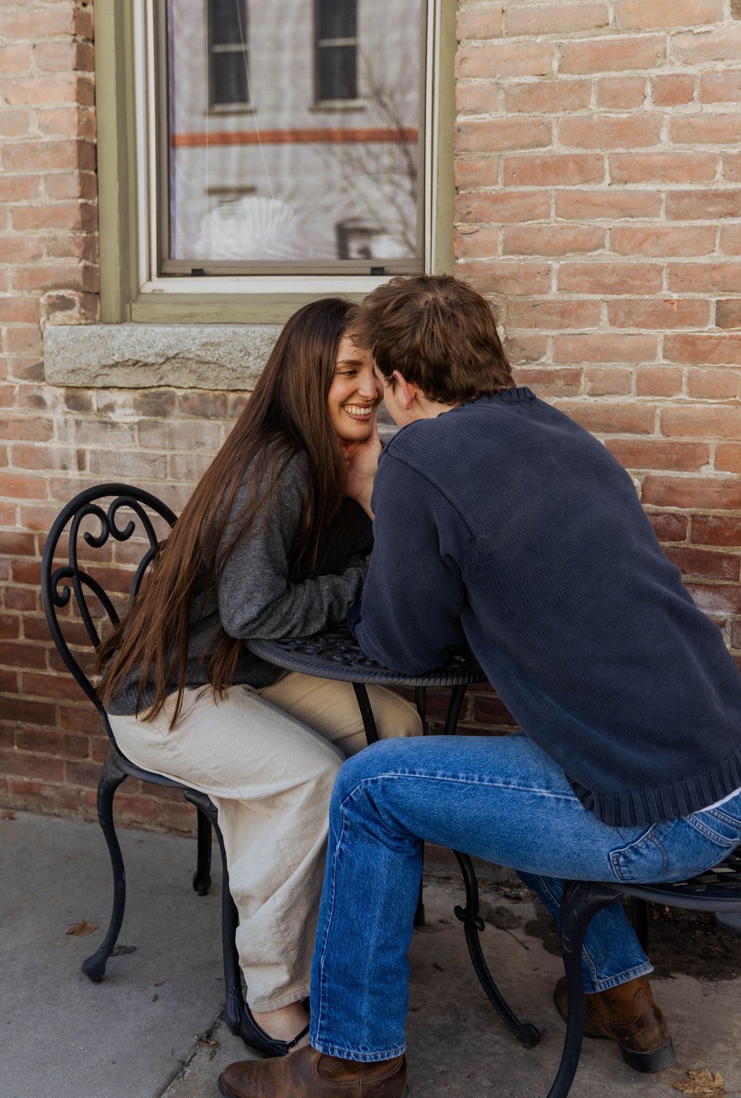 A couple sharing a sweet moment while sitting on a wrought iron bench near a brick wall.