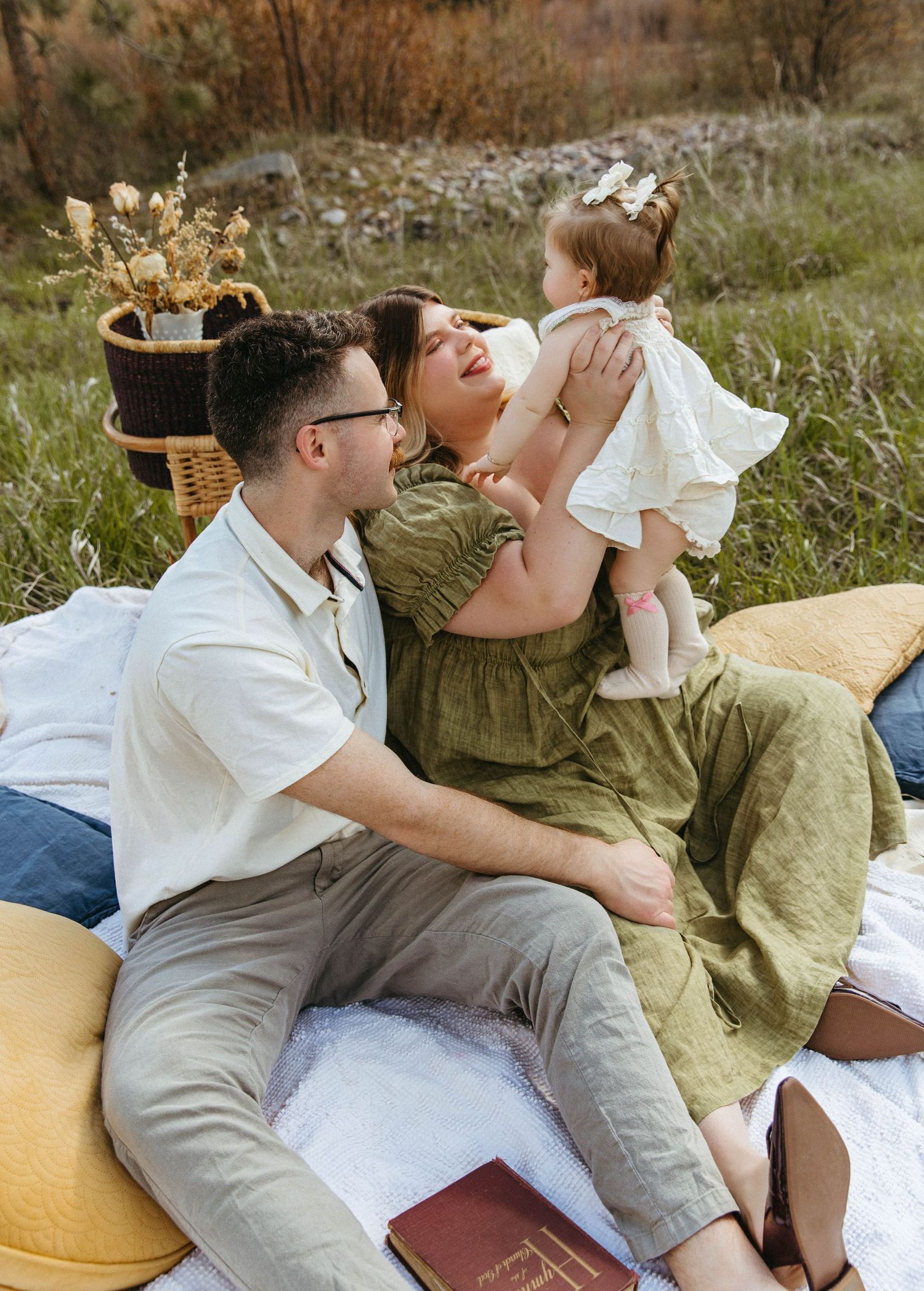 A couple lounges together in casual attire on pillows in a grassy outdoor setting during a picnic.